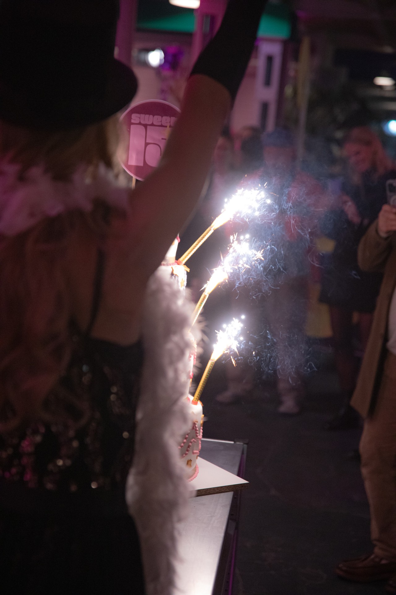 Feierliche Szene mit einer Person, die einen Kuchen mit glitzernden Feuerwerkskörpern präsentiert.
