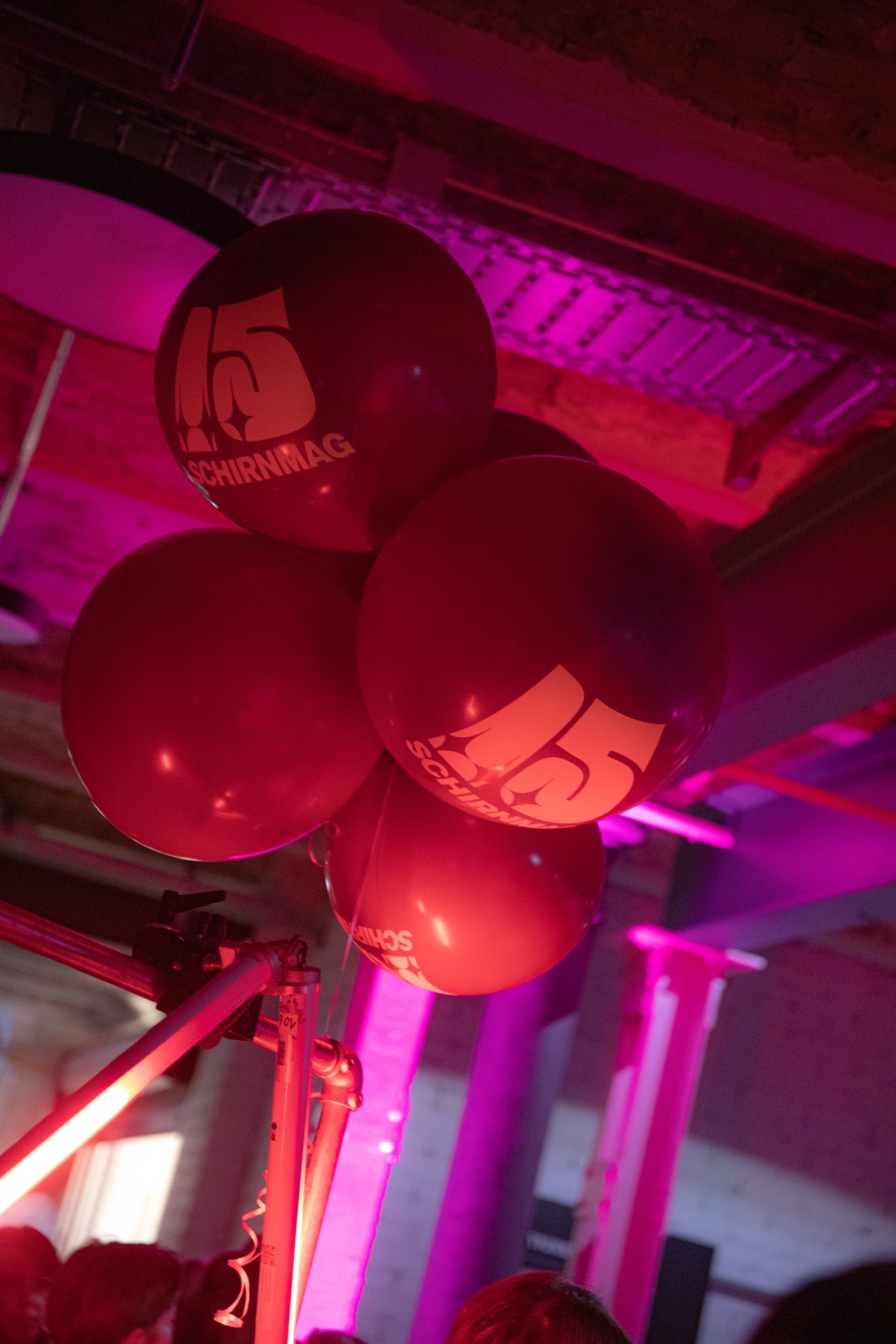 Rote Ballons mit "15 SCHIRNMAG"-Aufdruck in einer Eventlocation, die von pinkem Licht beleuchtet wird.