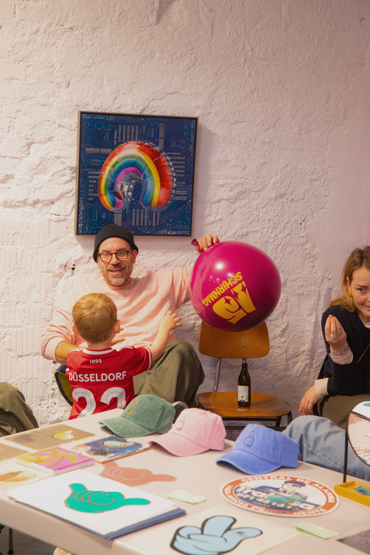 Vater und Sohn in einem kreativen Raum, umgeben von Hüten, Spielzeug und einem bunten Wandgemälde.