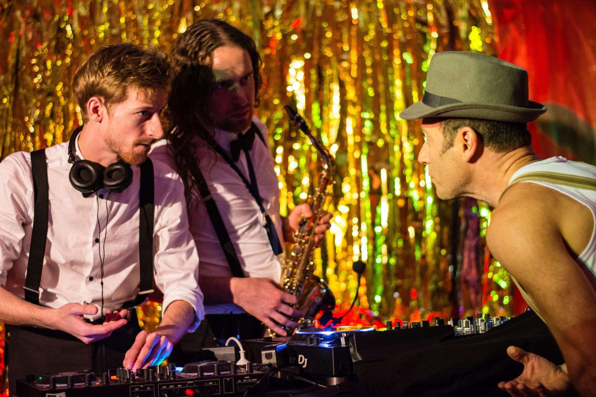 Three musicians interact on a festive stage, surrounded by sparkling decorations and musical instruments.