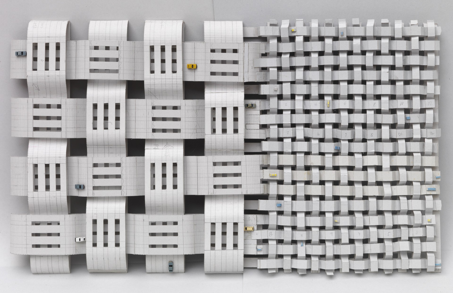 Moderne Papierstadt aus geflochtenen Streifen mit Miniaturautos vor neutralem Hintergrund.