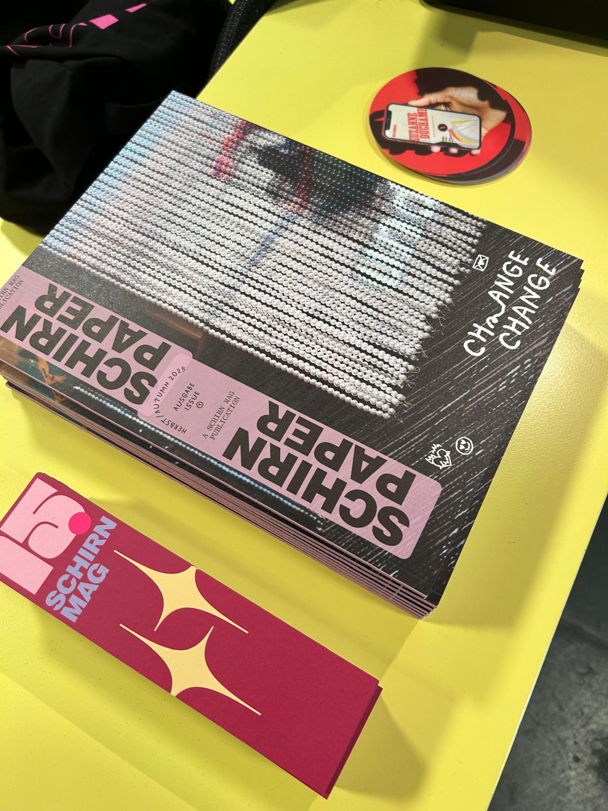 Stapel von Magazinen mit dem Titel "Schirn Paper" und einem pinken Lesezeichen auf einem gelben Tisch.