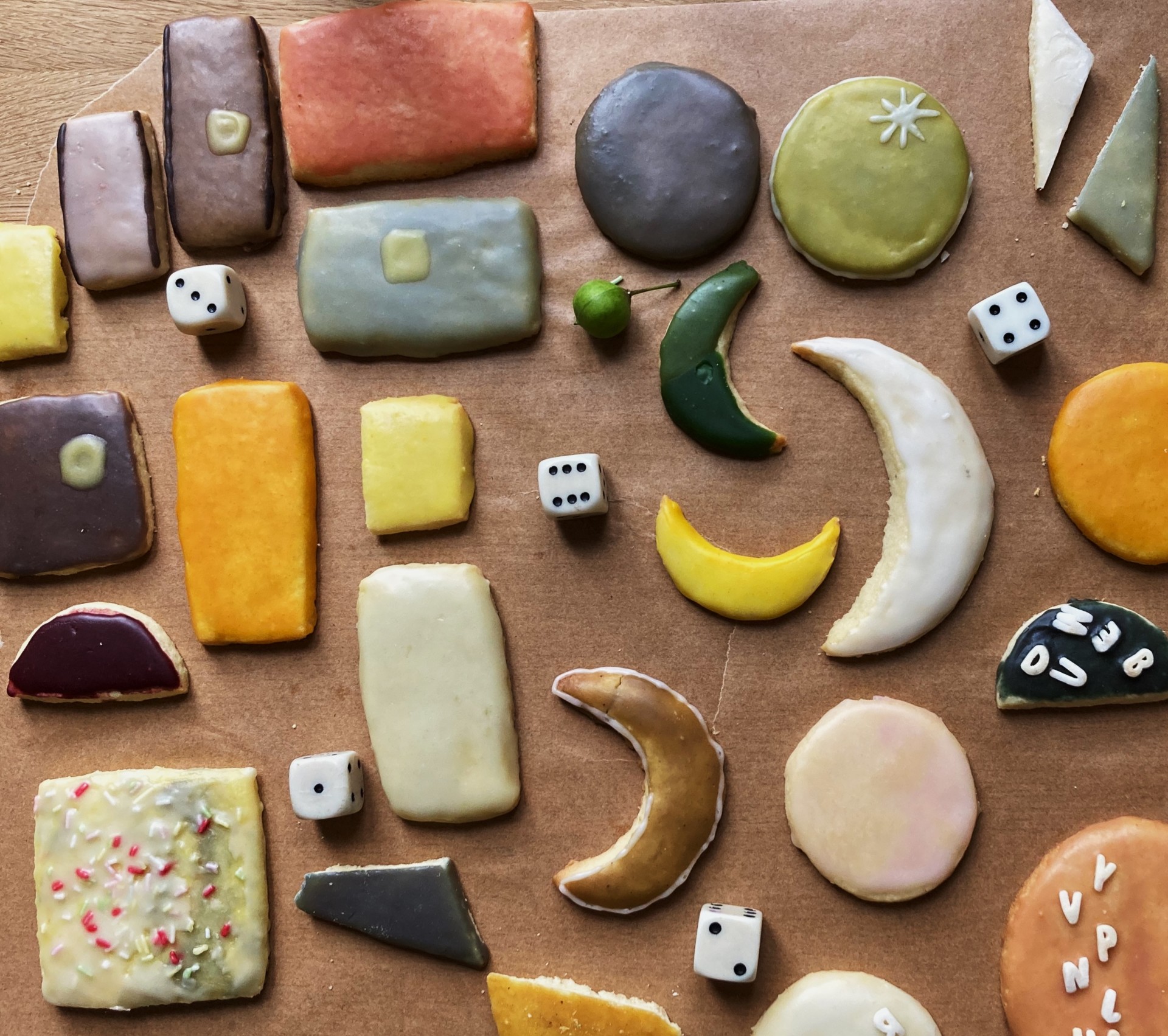 Bunte, dekorierte Kekse in verschiedenen Formen und Farben auf braunem Papier verteilt.