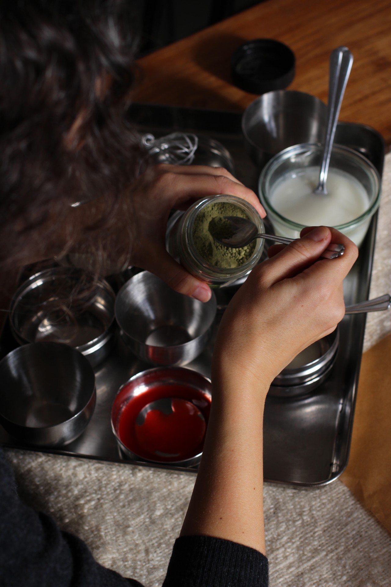 A person mixes various ingredients in a bowl on a table with metal containers and spoons.