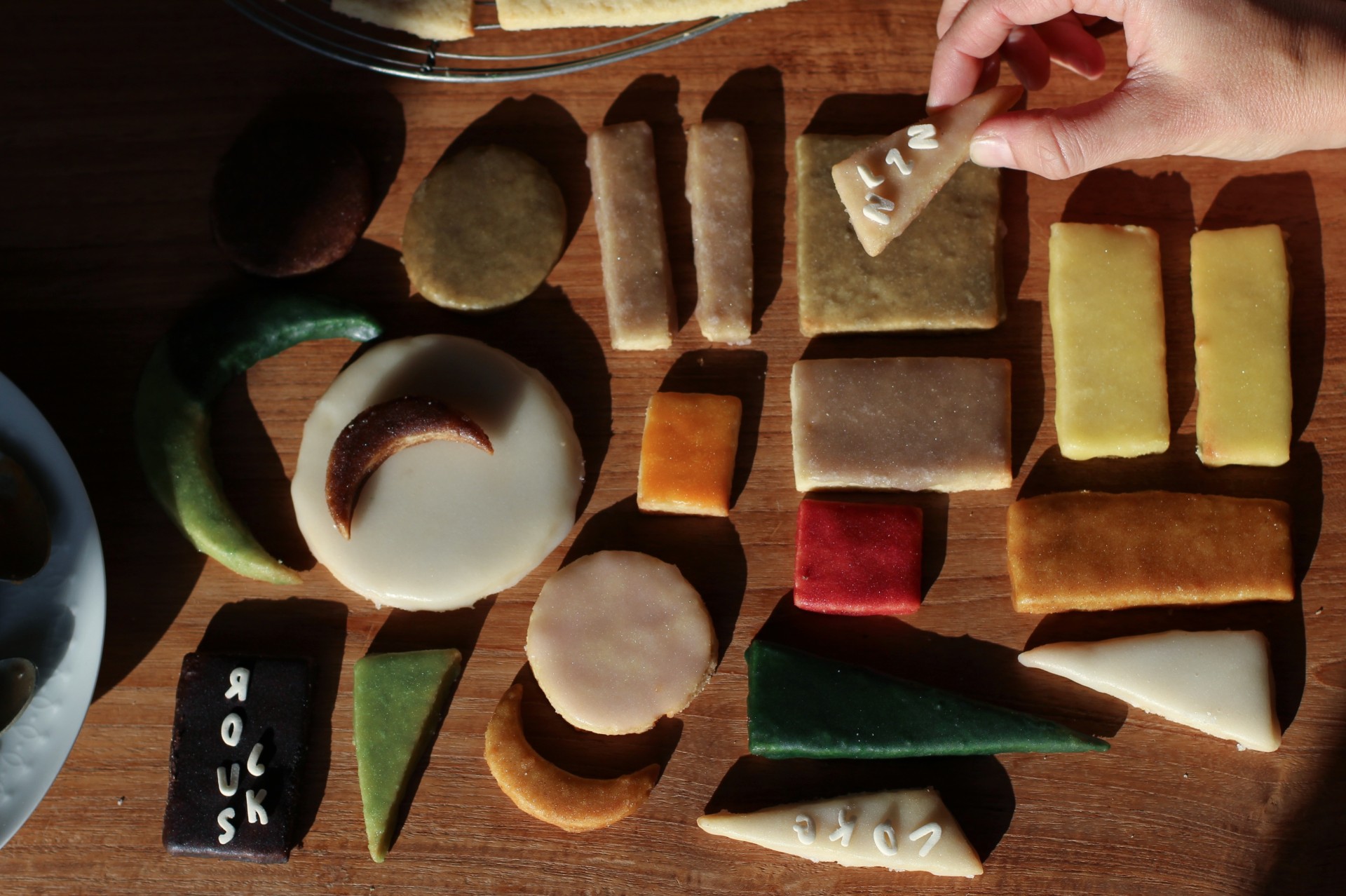 Colorful, geometrically shaped cookies are on a wooden board, some decorated with inscriptions.