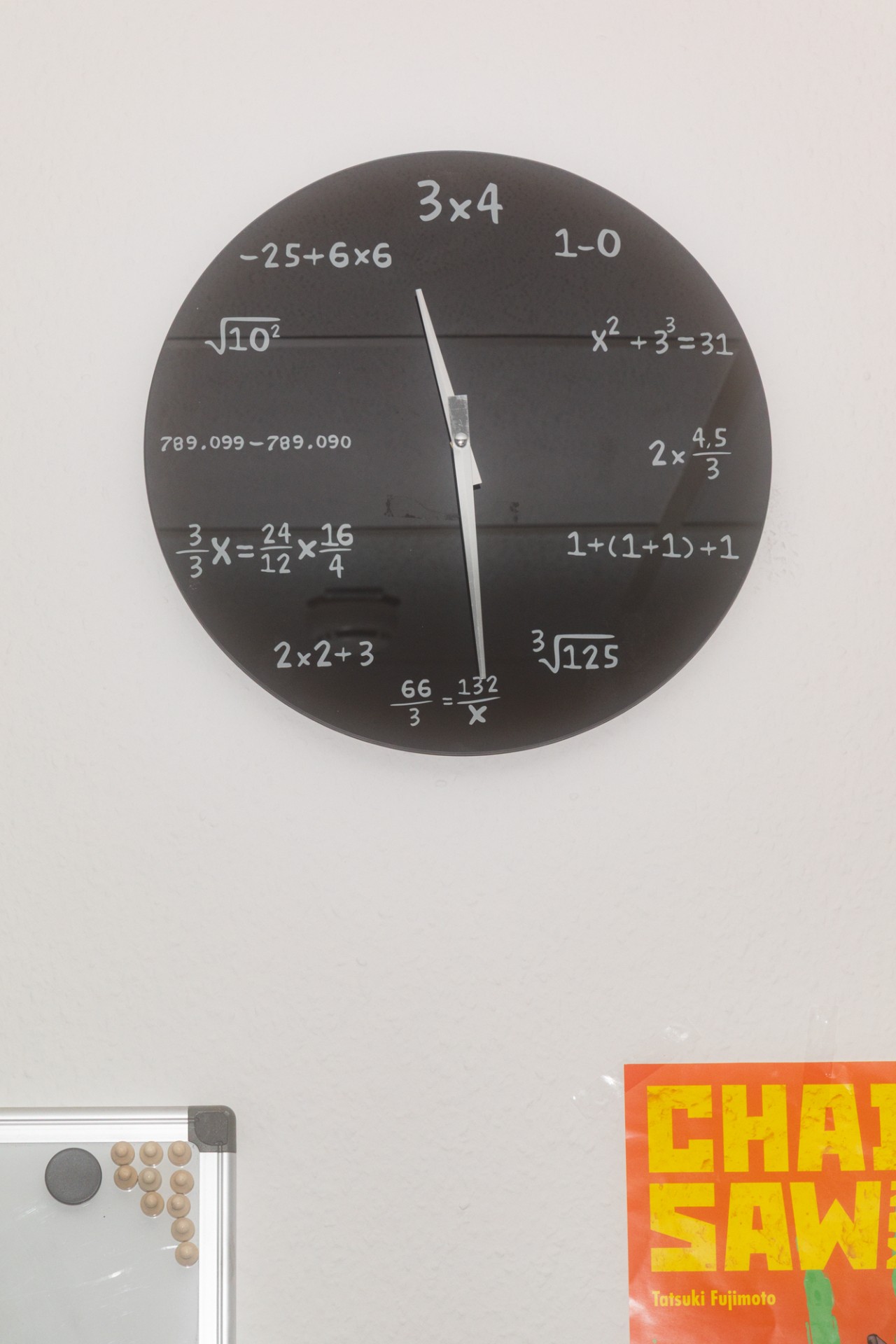 Schwarze Wanduhr mit mathematischen Formeln und Gleichungen als Ziffern auf weißem Hintergrund.