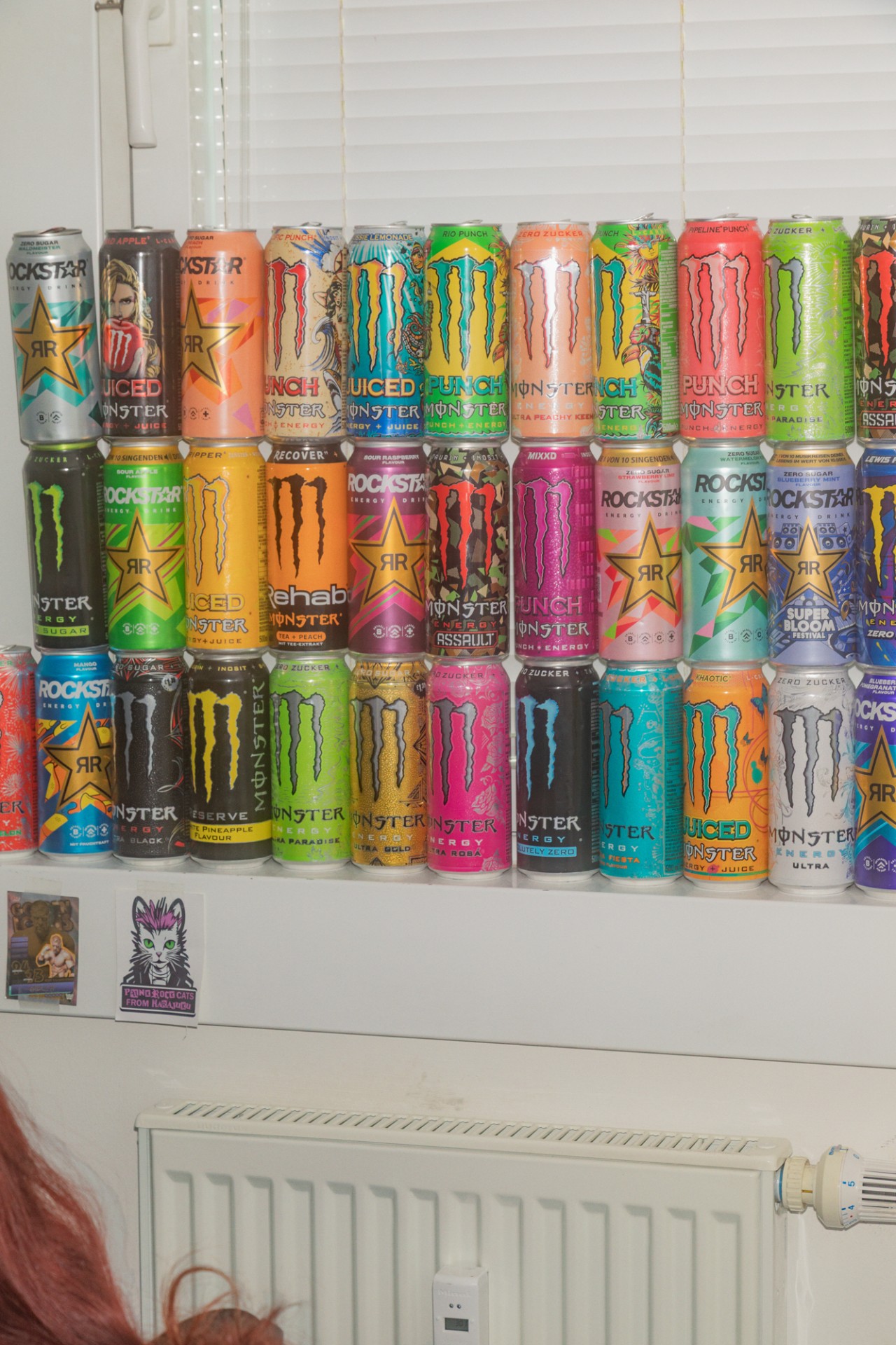 Bunte Sammlung von Energy-Drink-Dosen, darunter Marken wie Monster und Rockstar, an einer Wand angeordnet.