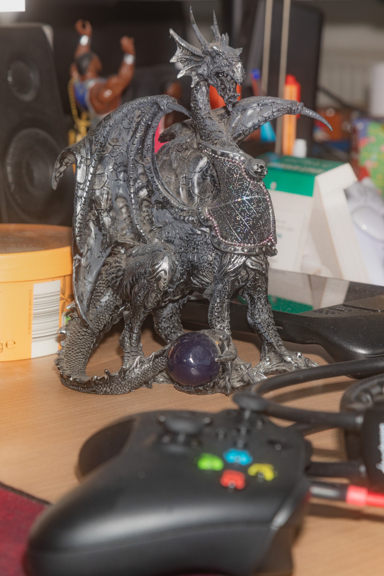 Detaillierte Drachenfigur mit Flügeln und Kristall, umgeben von Gaming-Zubehör und Alltagselementen.