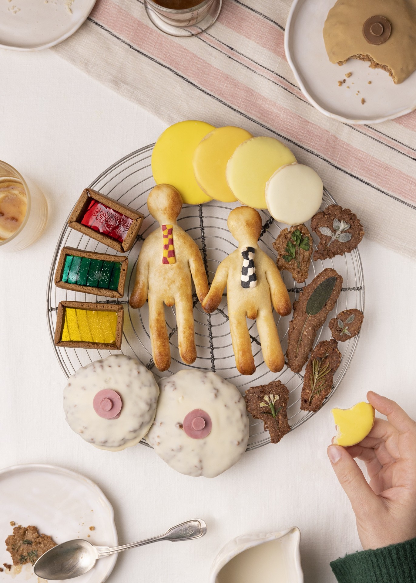 Bunt dekorierte Plätzchen in Figuren- und geometrischen Formen auf einem Gitterrost, umgeben von weiteren Süßigkeiten.