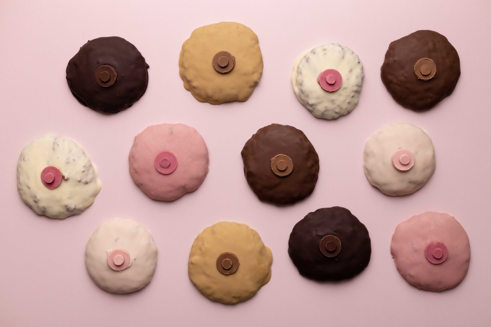 Bunte Schokoladenkekse in verschiedenen Farben, auf einem rosa Hintergrund arrangiert.