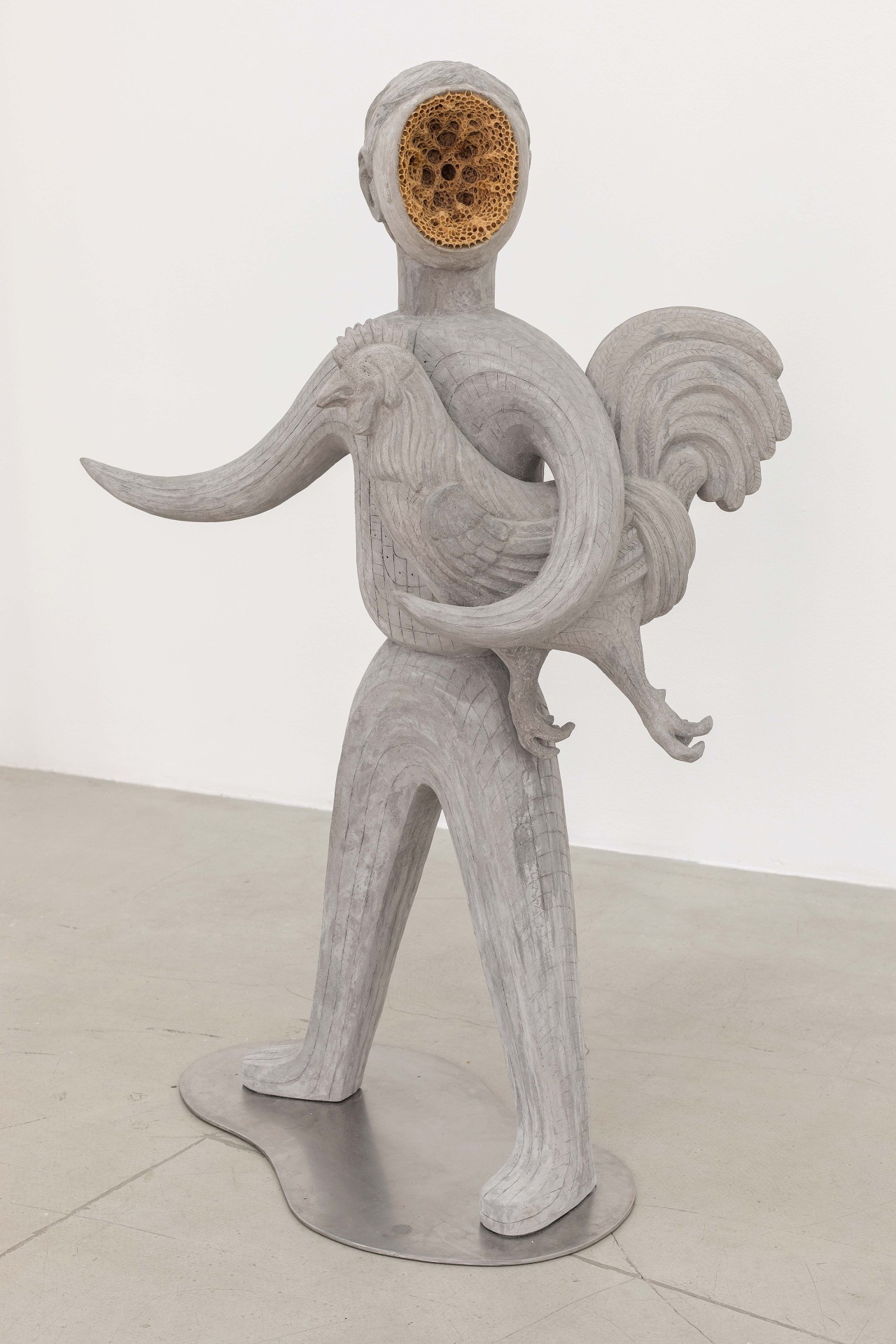Skulptur einer menschlichen Figur mit hohlem Kopf, die ein Huhn trägt, aus grauem Material, moderne Kunst.