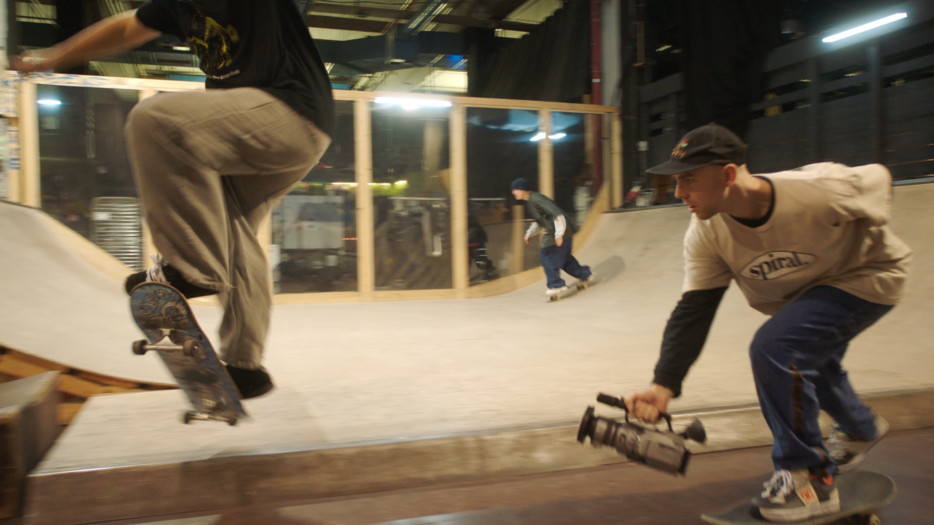 Skater springt über eine Rampe, während ein anderer mit einer Kamera filmt. Nachtstimmung im Skatepark.
