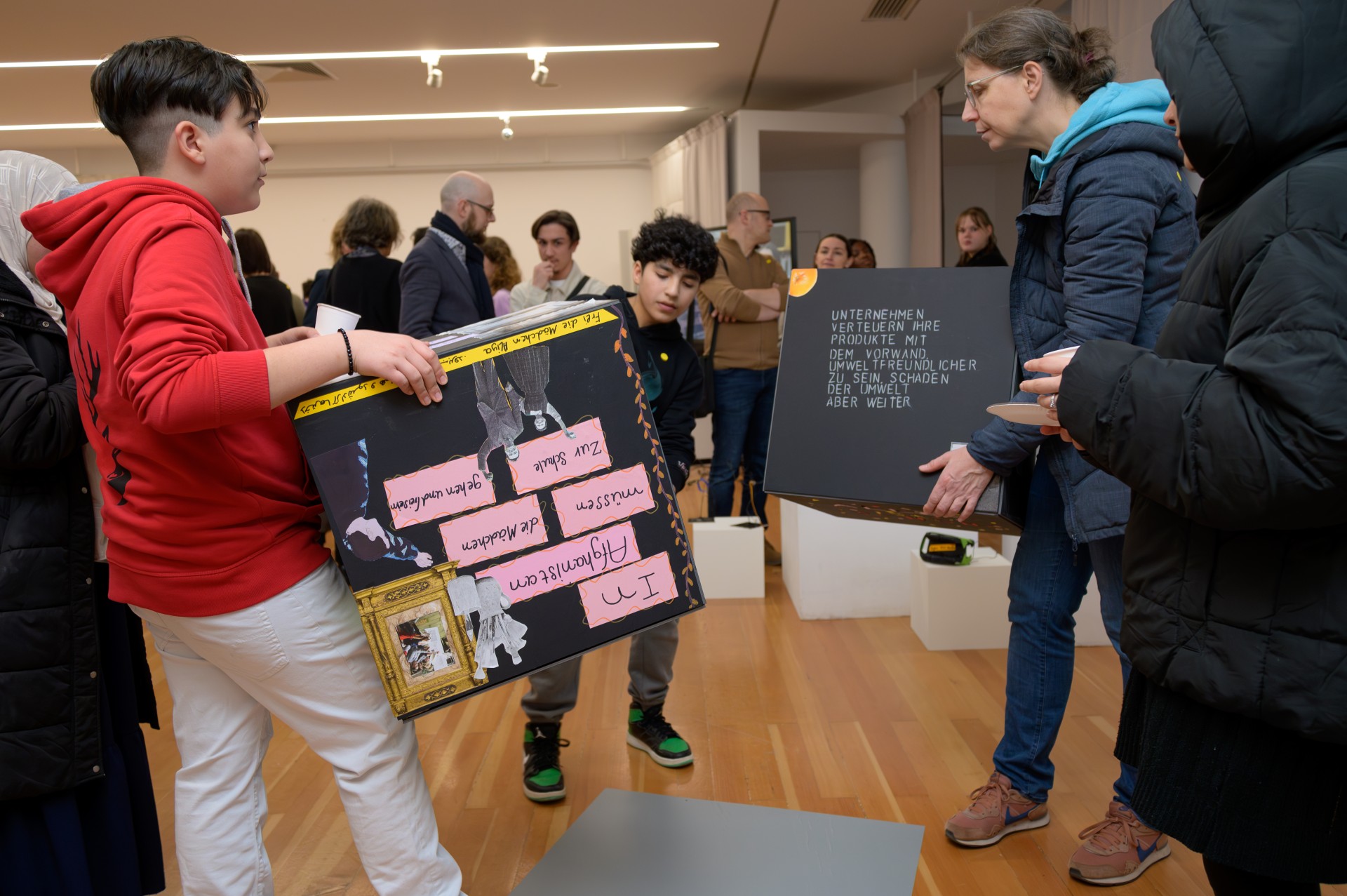 Kinder und Erwachsene in einer Ausstellung, tragen Kisten mit Infos. Veranstaltung zum Thema Umweltbewusstsein.