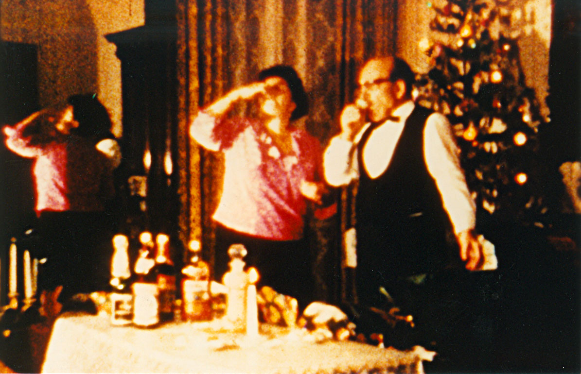 Feierliche Stimmung: Menschen stehen mit Getränken an einem Tisch, im Hintergrund strahlt ein geschmückter Weihnachtsbaum.