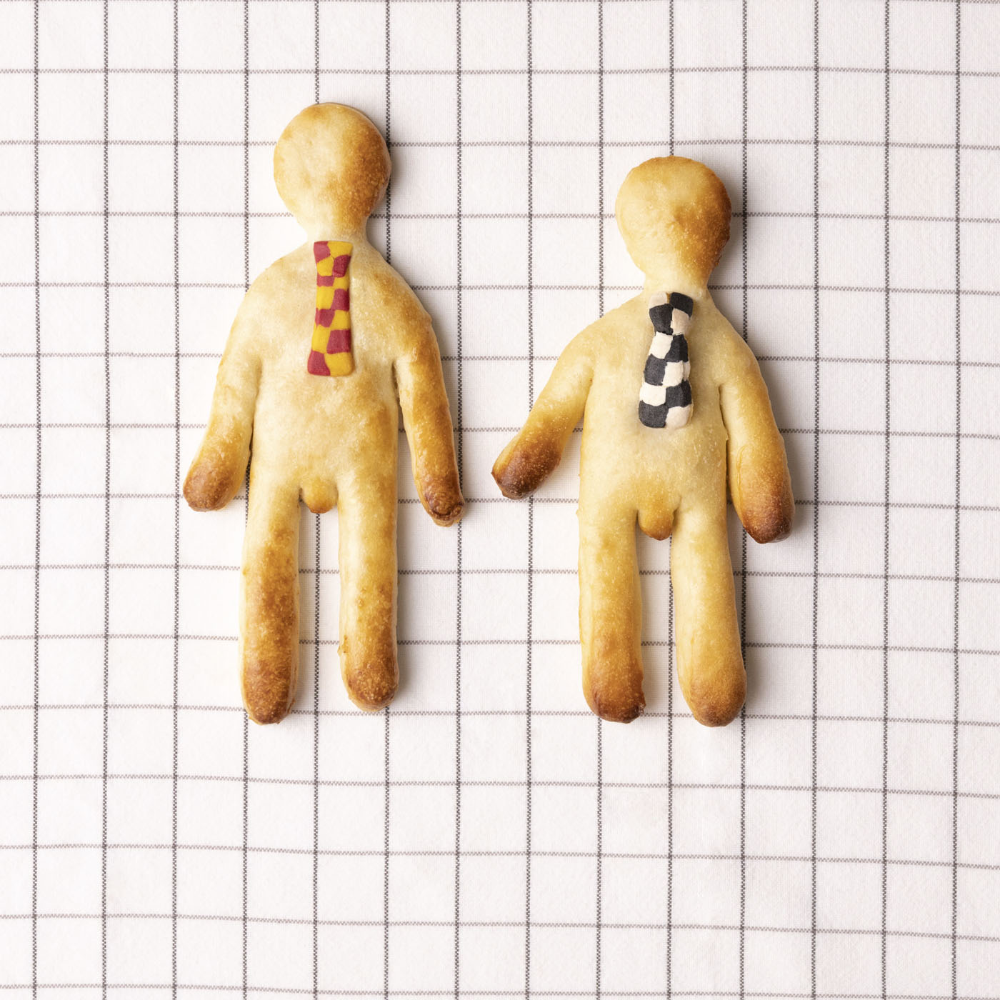 Zwei aus Teig geformte Figuren mit bunten Krawatten vor einem karierten Hintergrund.