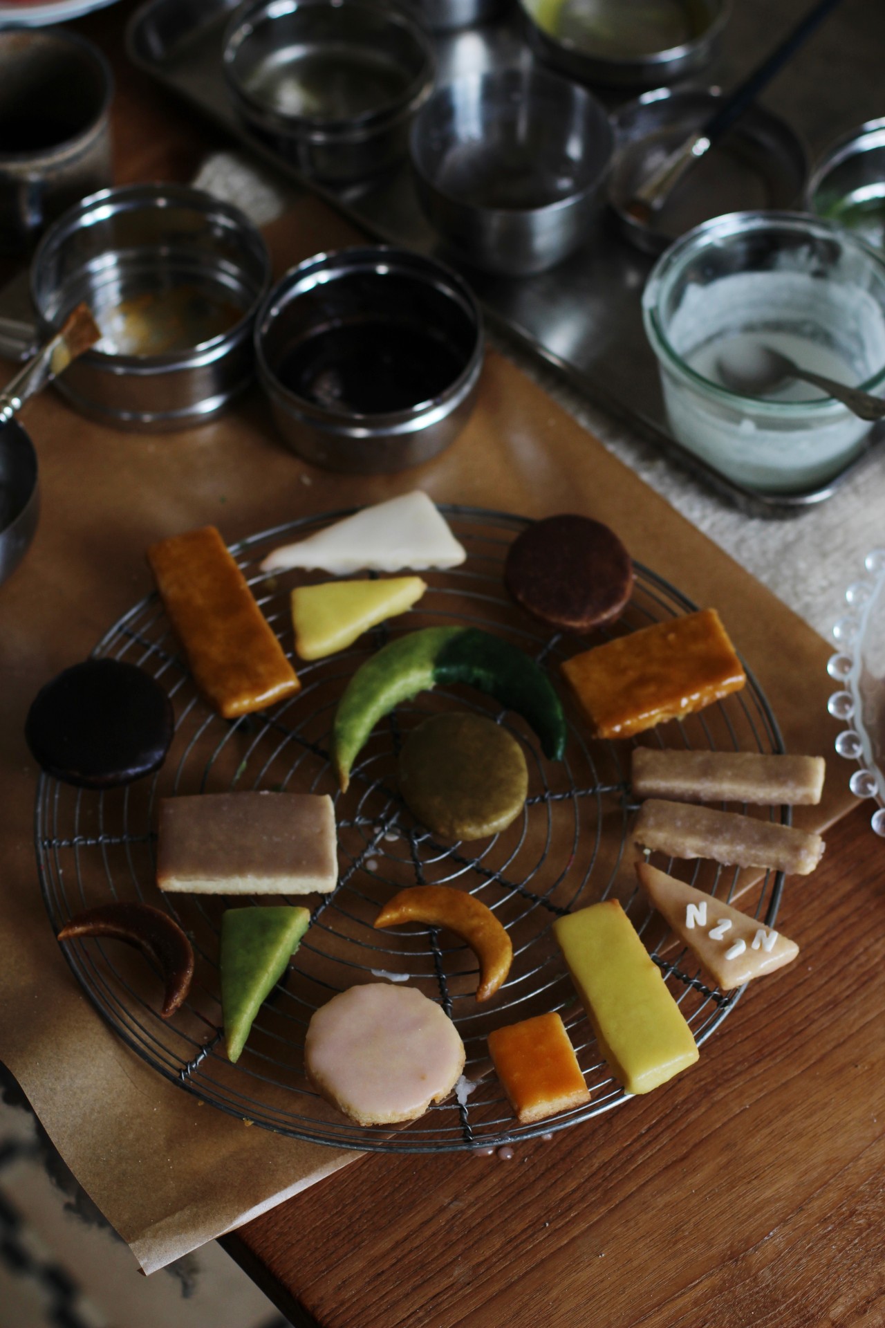 Colorfully decorated cookies on a rack, surrounded by various bowls of icing and ingredients.