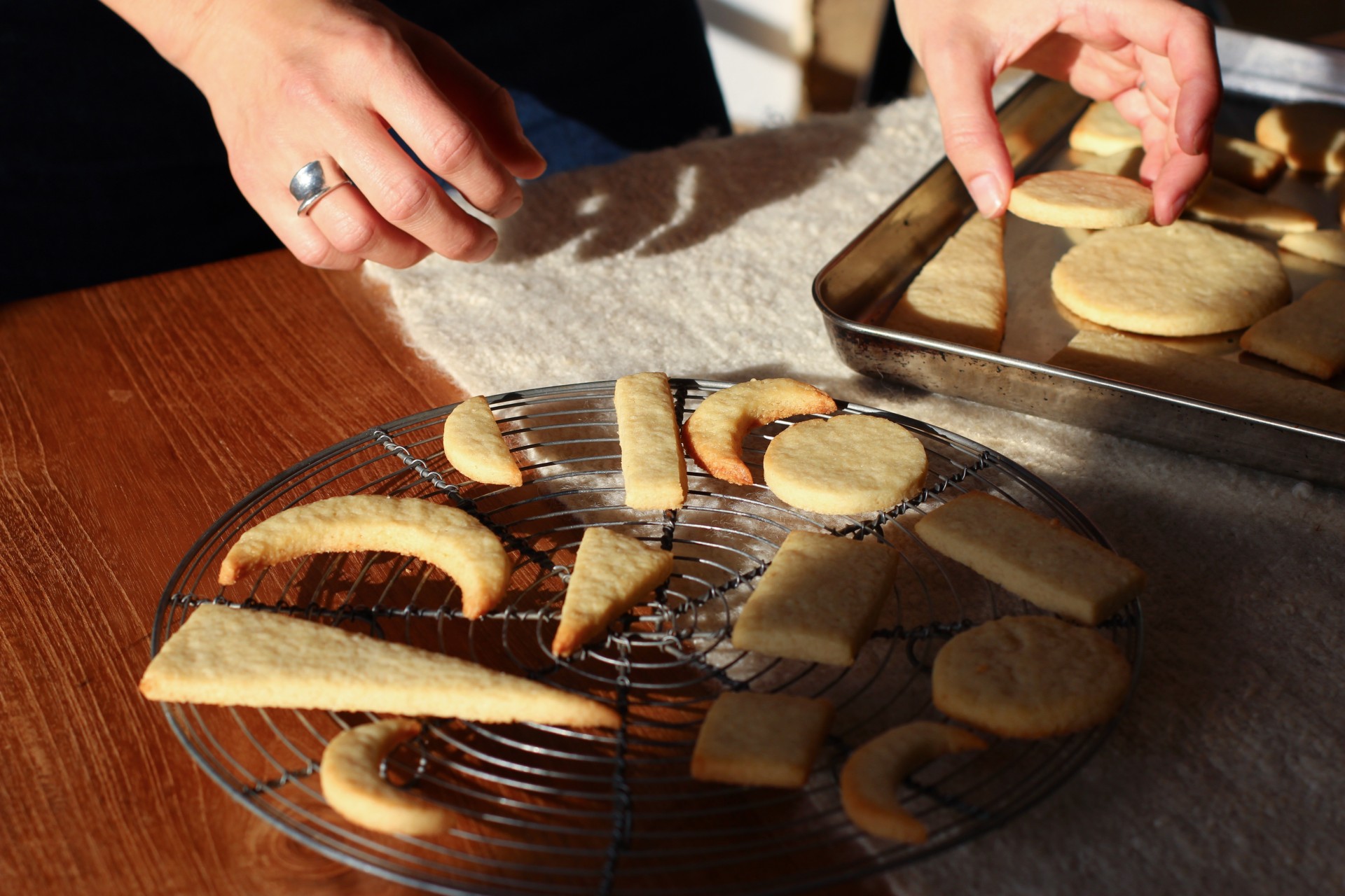 Hands place freshly baked cookies on a cooling rack to let them cool.