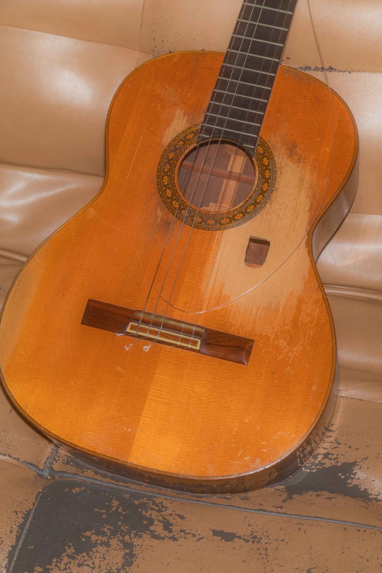 Eine gebrauchte akustische Gitarre liegt auf einem braunen Sofa.