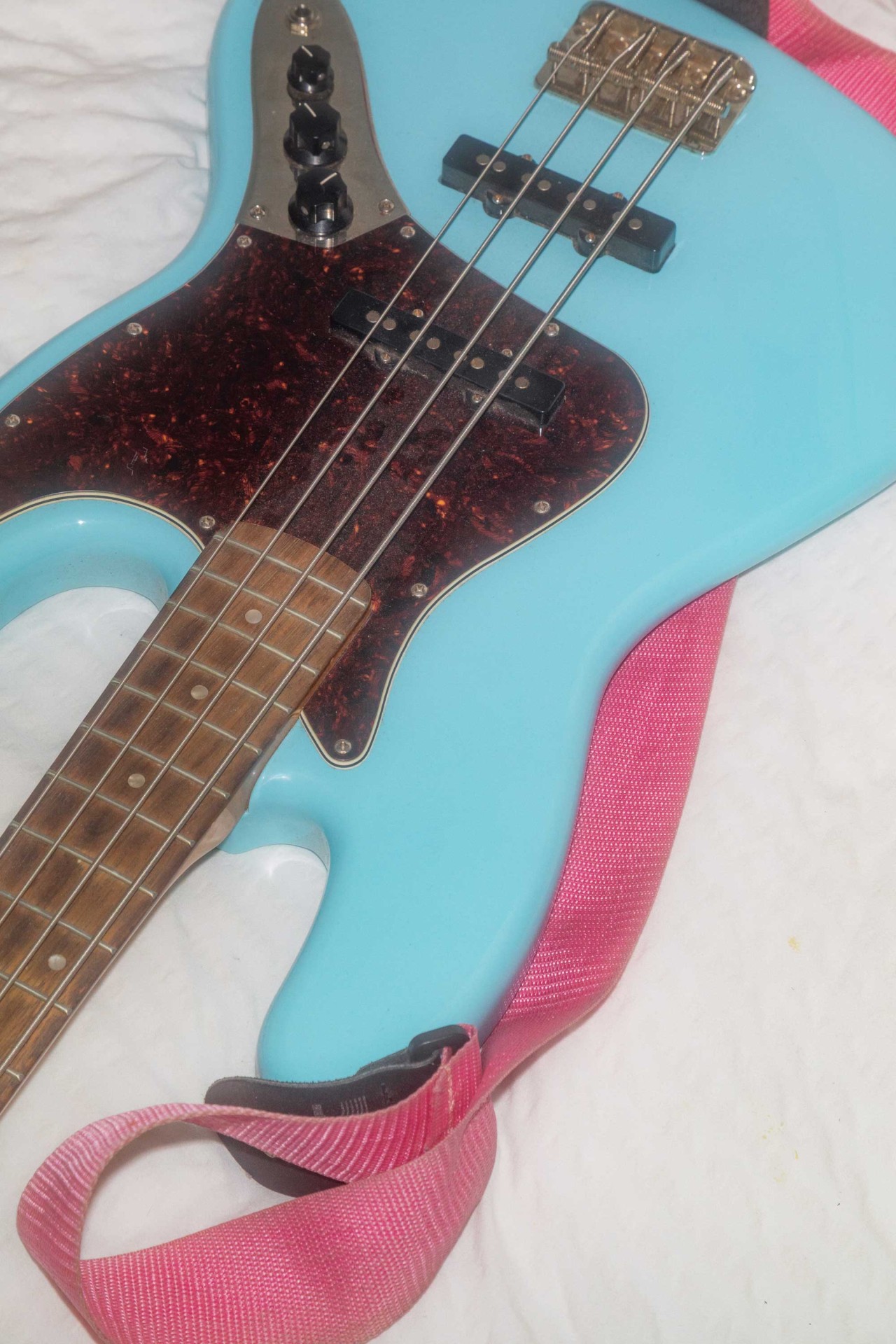 Nahaufnahme eines blauen E-Basses mit pinkem Gurt vor weißem Hintergrund.