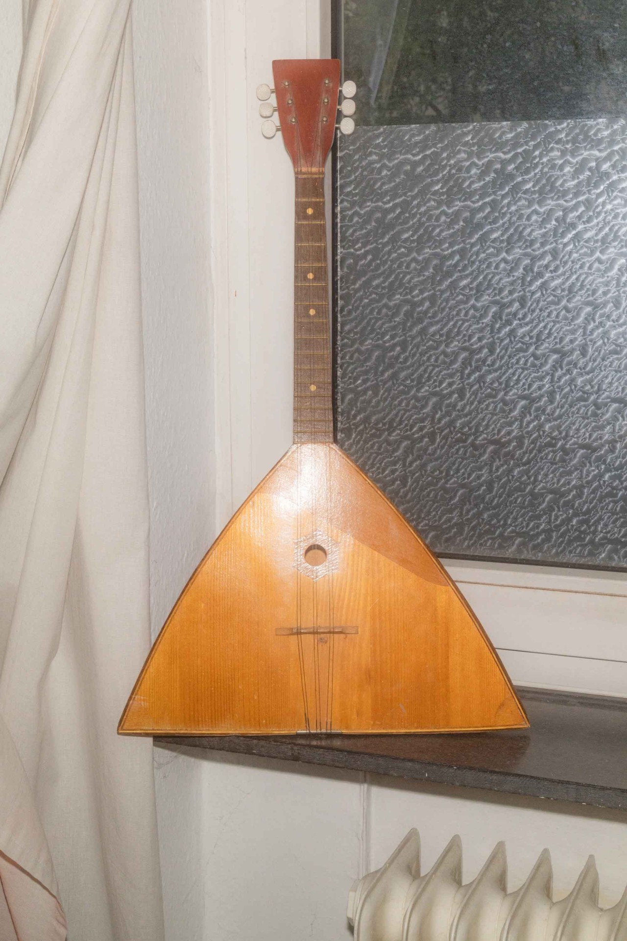 Traditionelles Musikinstrument mit dreieckigem Korpus, auf einem Tisch in Fensternähe platziert.