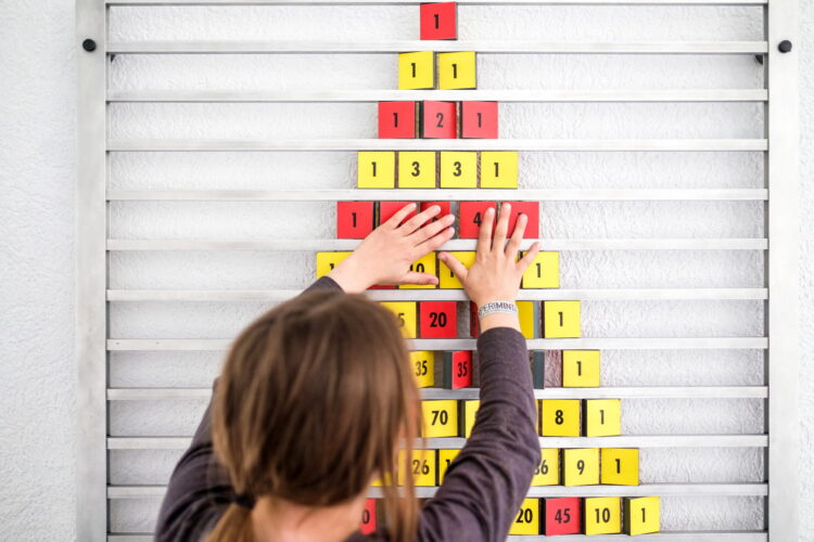 Kind gestaltet farbige Zahlenblöcke zu einem Weihnachtsbaum an der Wand.