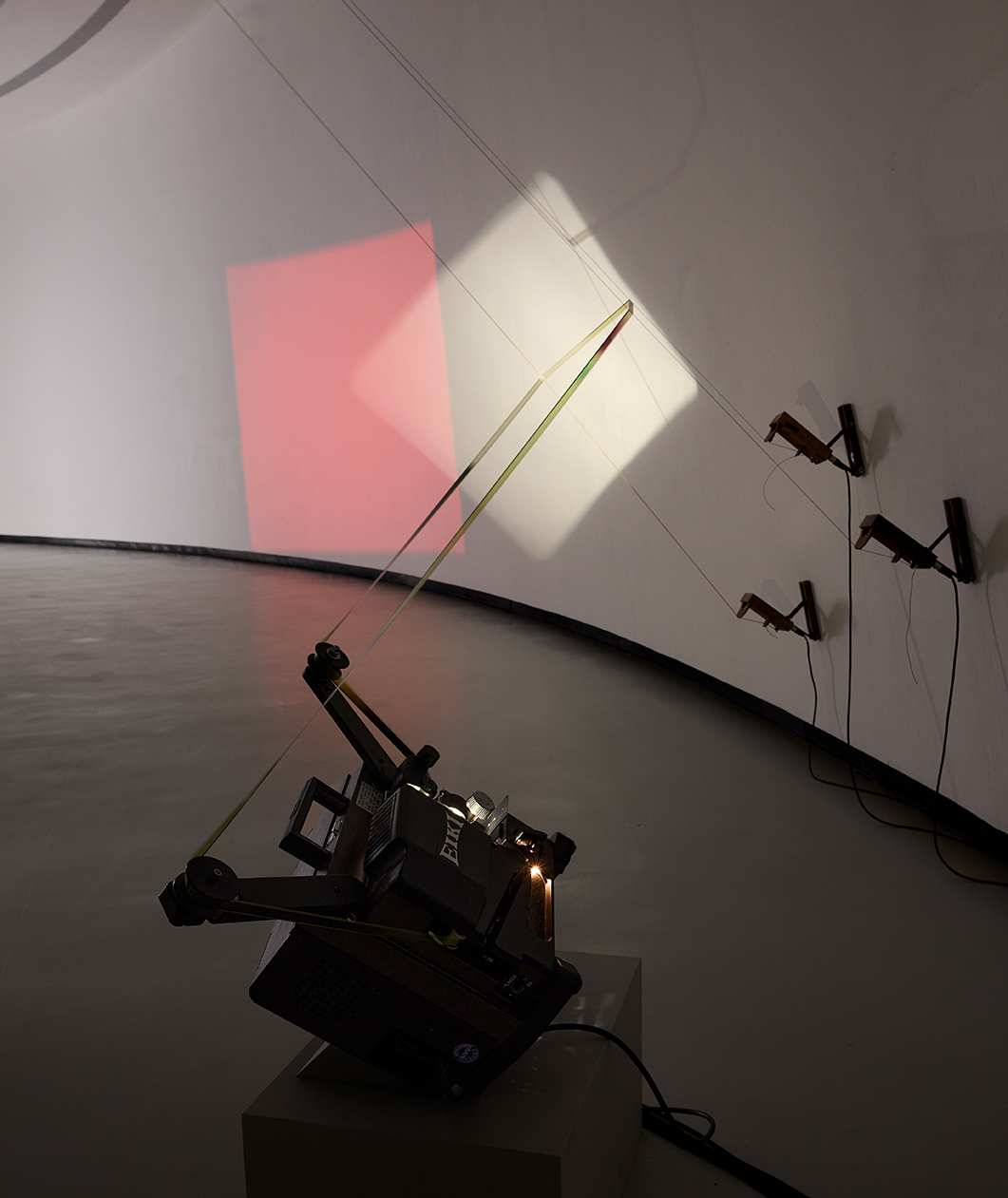 Installation mit Projektor, der Lichtstrahlen auf eine gebogene Wand projiziert, ergänzt durch grafische Elemente.