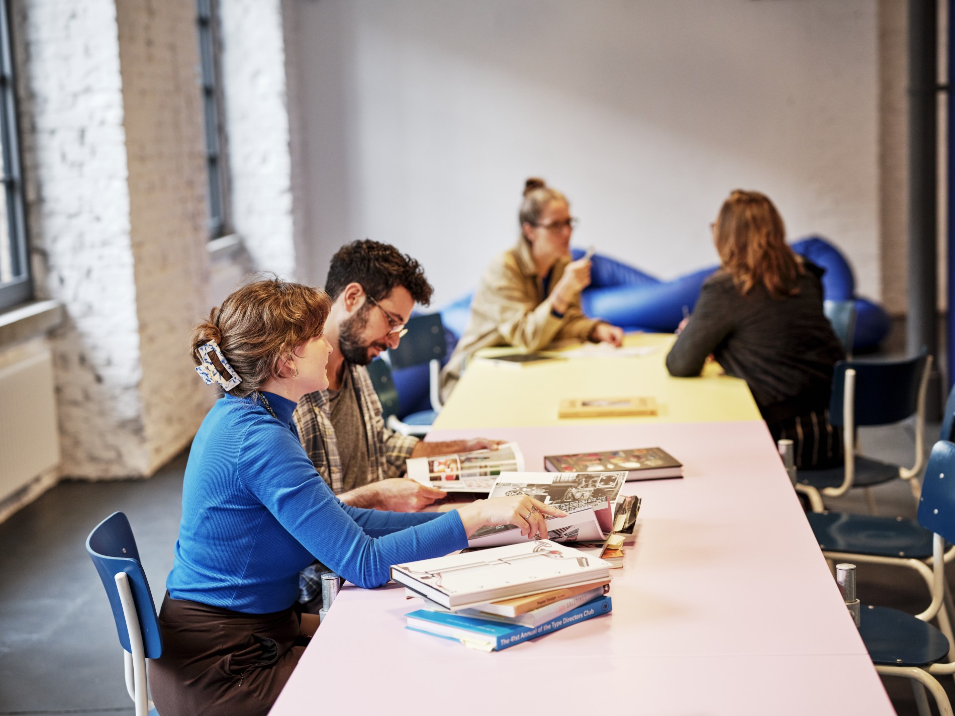 Vier Personen sitzen an einem bunten Tisch, blättern in Büchern und unterhalten sich.
