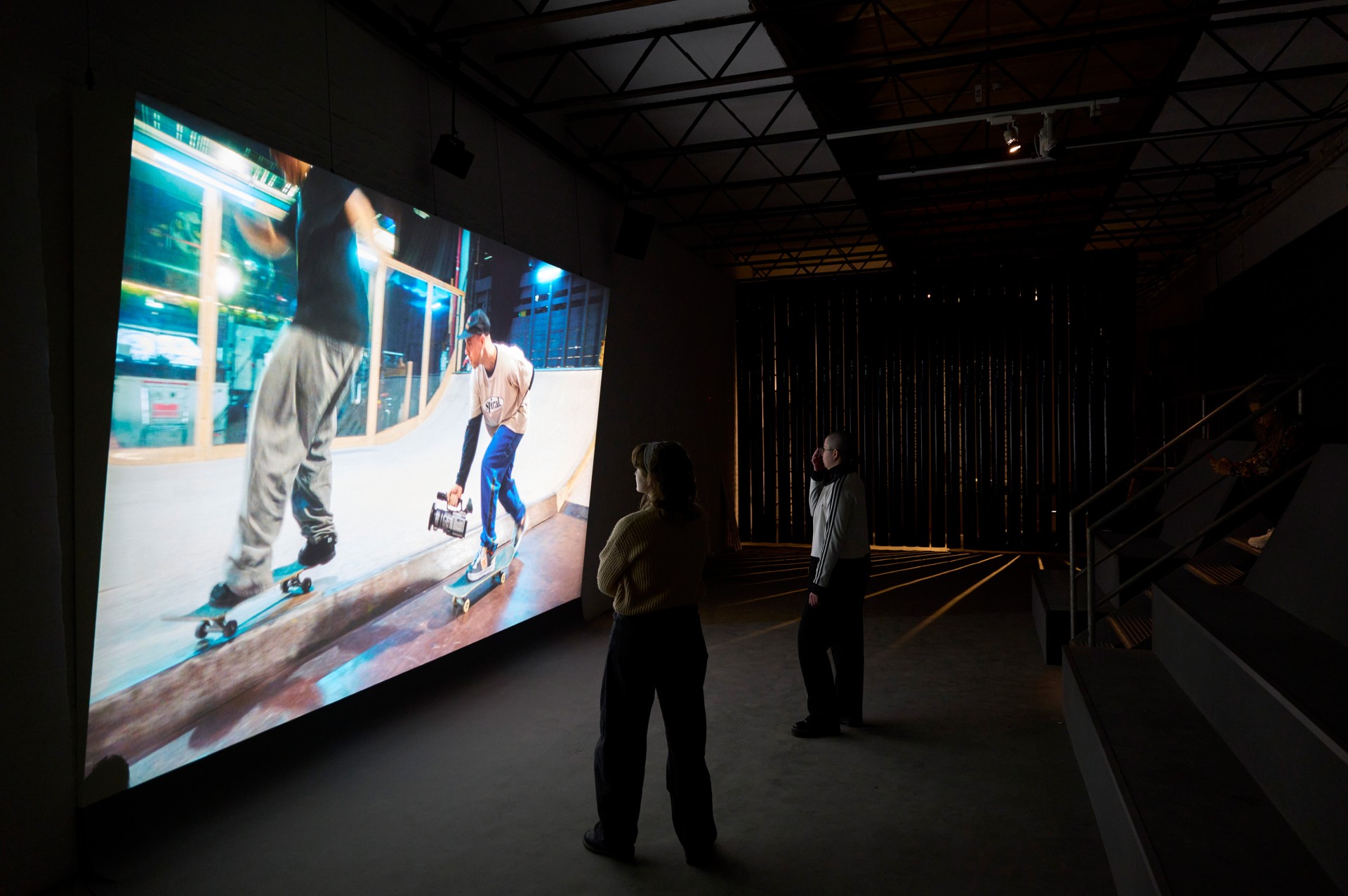 Skater auf großer Leinwand, Betrachter im Raum, szenische Atmosphäre mit moderner Beleuchtung.