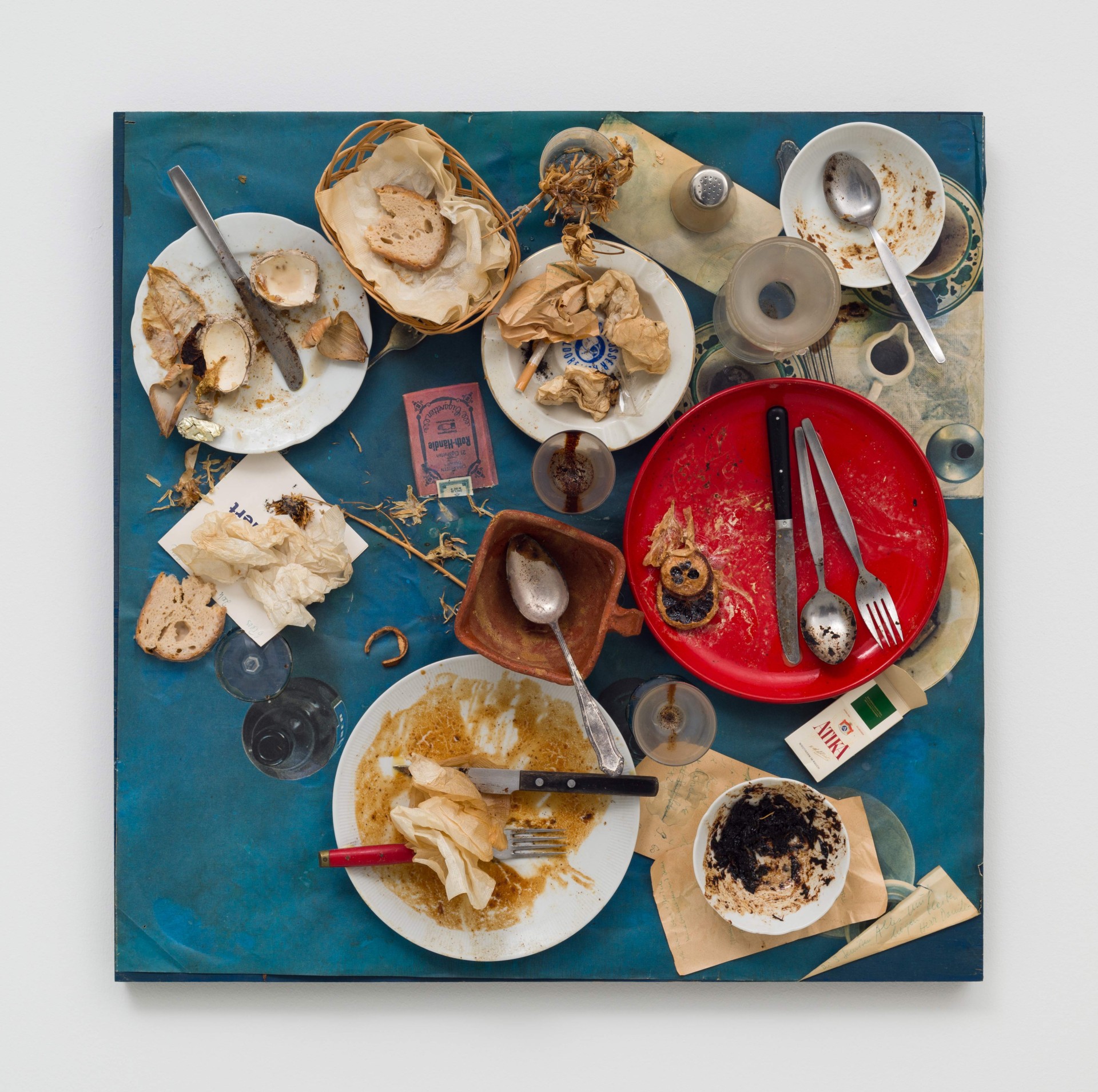 Crowded table with dirt-covered plates, cutlery, and food scraps on a blue tablecloth.