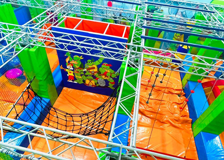 Bunte Indoor-Spielanlage mit Kletternetzen und Ninja-Turtle-Motiv, ideal für Kinder zum Spielen und Entdecken.