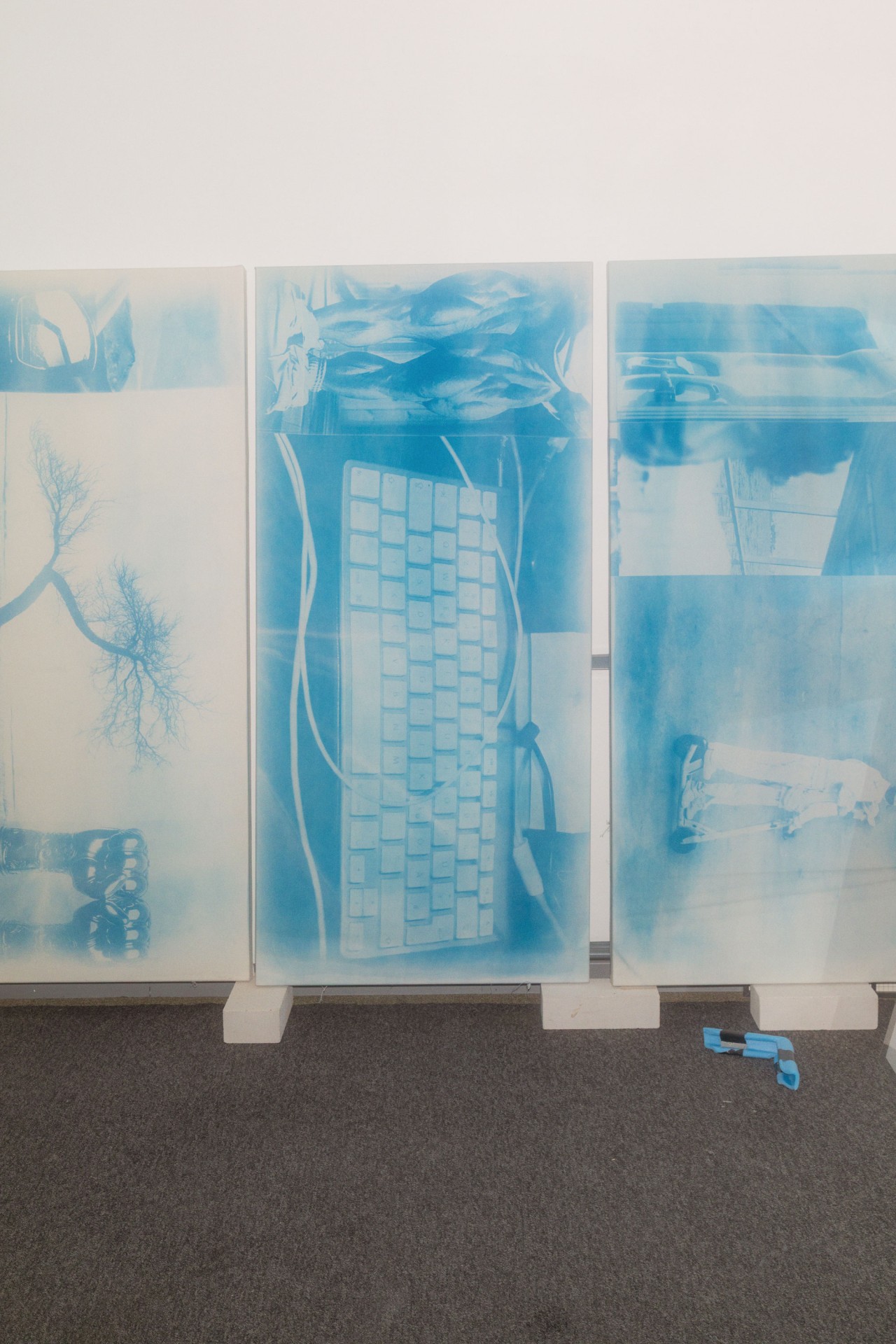 Drei transparente Platten mit blauen Bildern alltäglicher Gegenstände, darunter eine Tastatur und eine Baum-Silhouette.