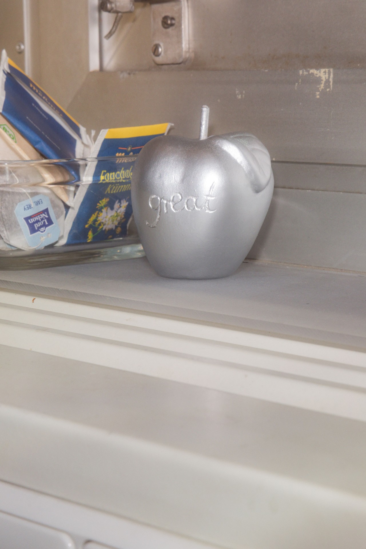 Silberner Apfel mit der Aufschrift "great" steht neben Teetüten auf einer Arbeitsfläche.