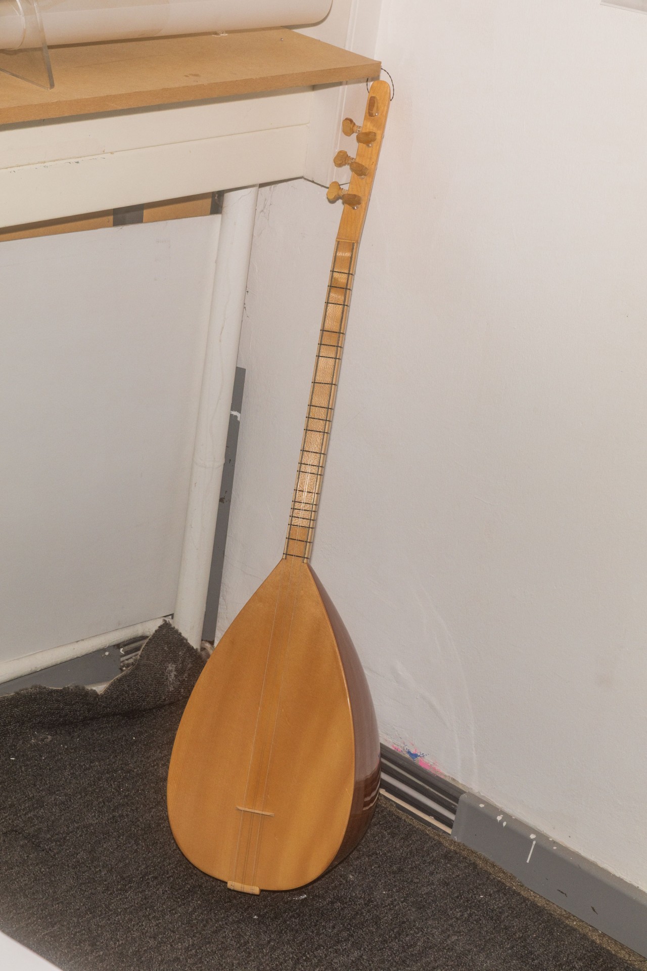 Ein traditionelles, helles Saiteninstrument mit birnenförmigem Korpus, an eine Wand gelehnt.