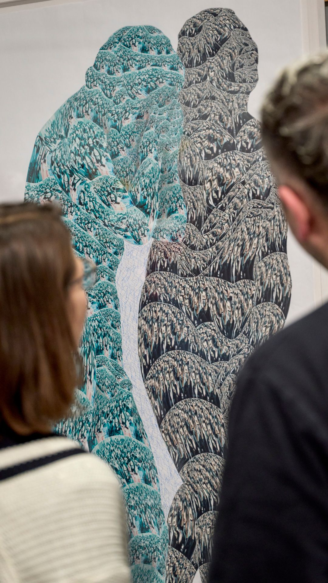 Zwei silhouettenartige Figuren aus bunten Mustern, beobachtet von zwei Personen in einem Kunstraum.