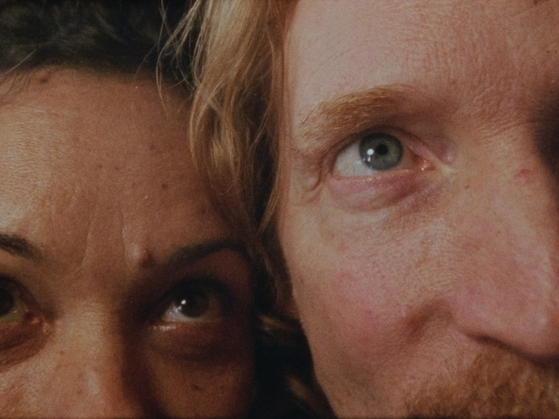 Nahaufnahme zweier Gesichter, die nebeneinander mit fokussierten Augen in die Kamera schauen. Intime Atmosphäre.