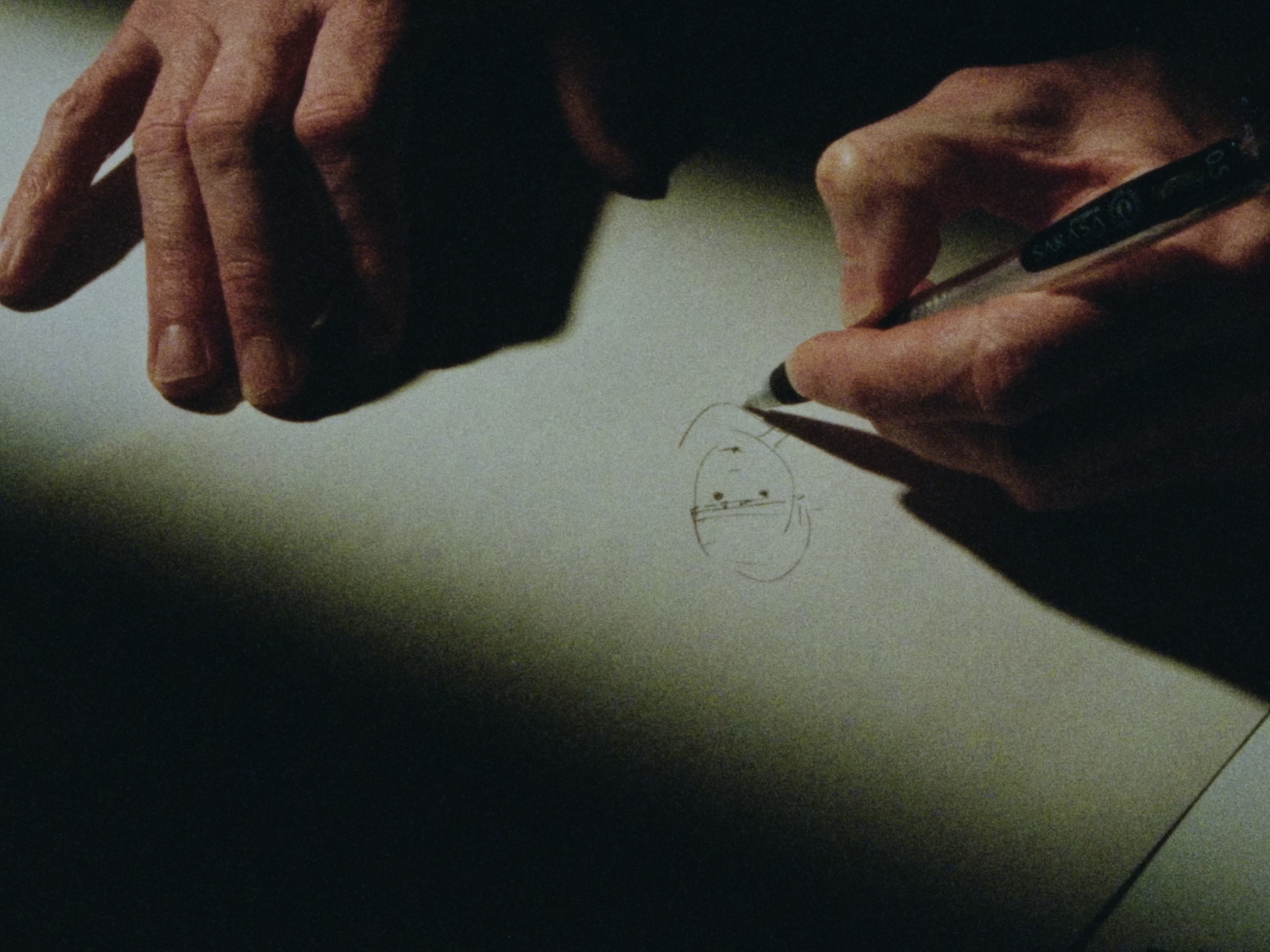 Eine Hand skizziert schwach beleuchtet mit einem Stift auf einem Blatt Papier.