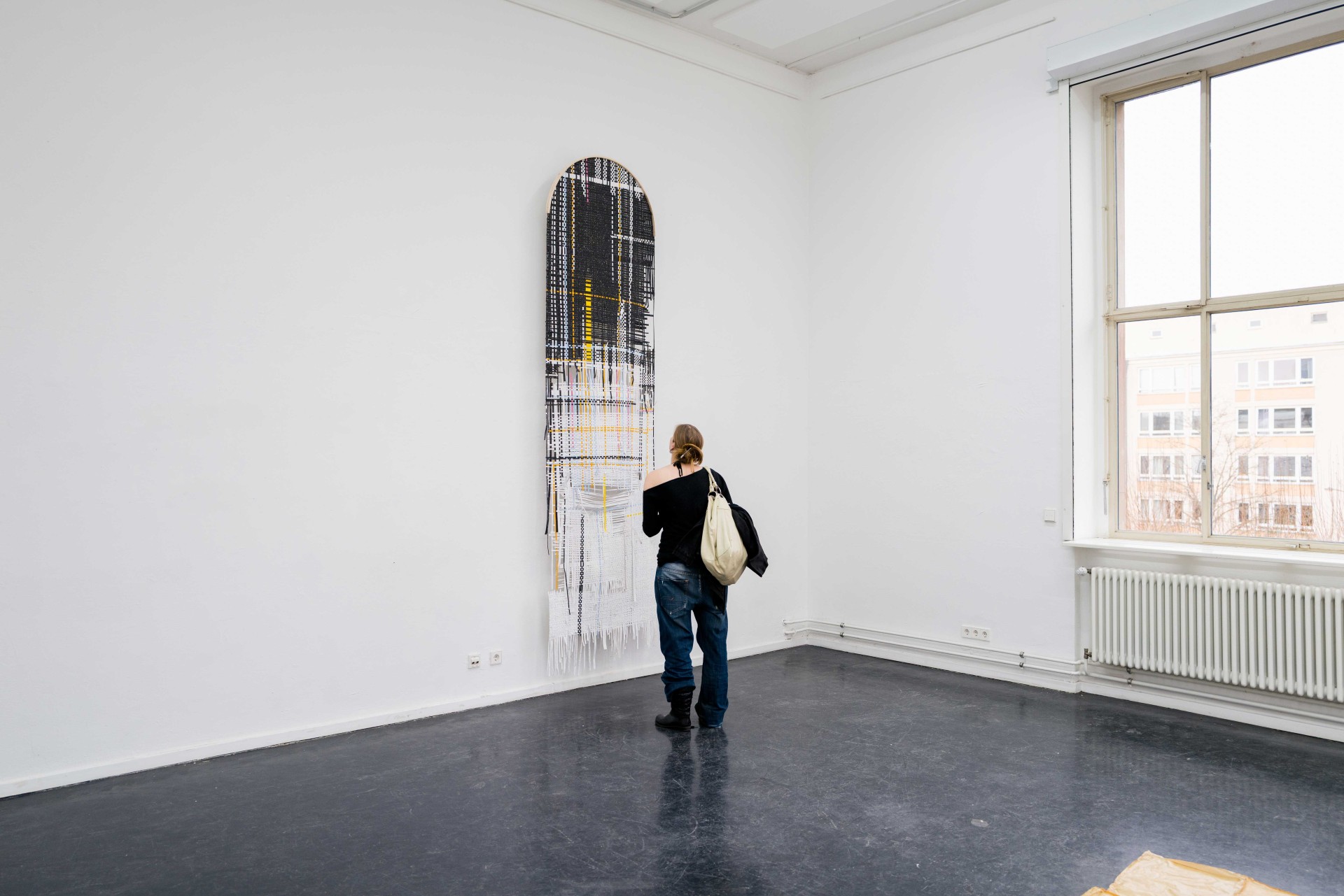 Person betrachtet ein abstraktes Kunstwerk in einem hellen, minimalistischen Raum mit großen Fenstern.