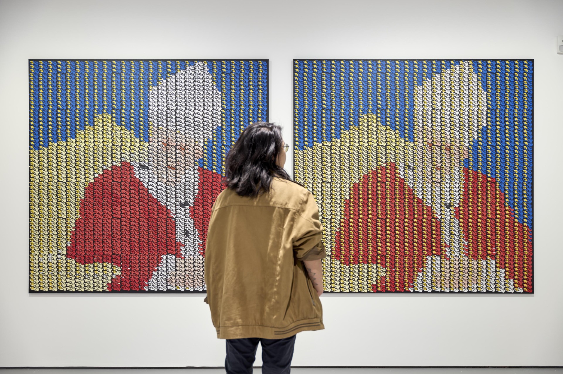 A person looks at two similar artworks with colorful, stacked elements on the wall.