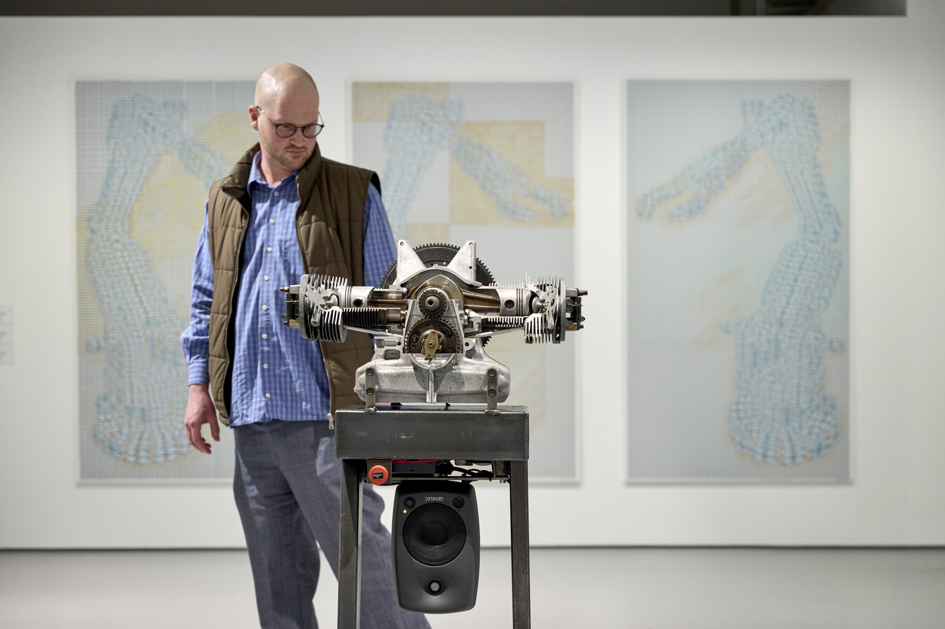 Ein Mann betrachtet eine technische Skulptur in der Galerie, während im Hintergrund abstrakte Kunstwerke zu sehen sind.