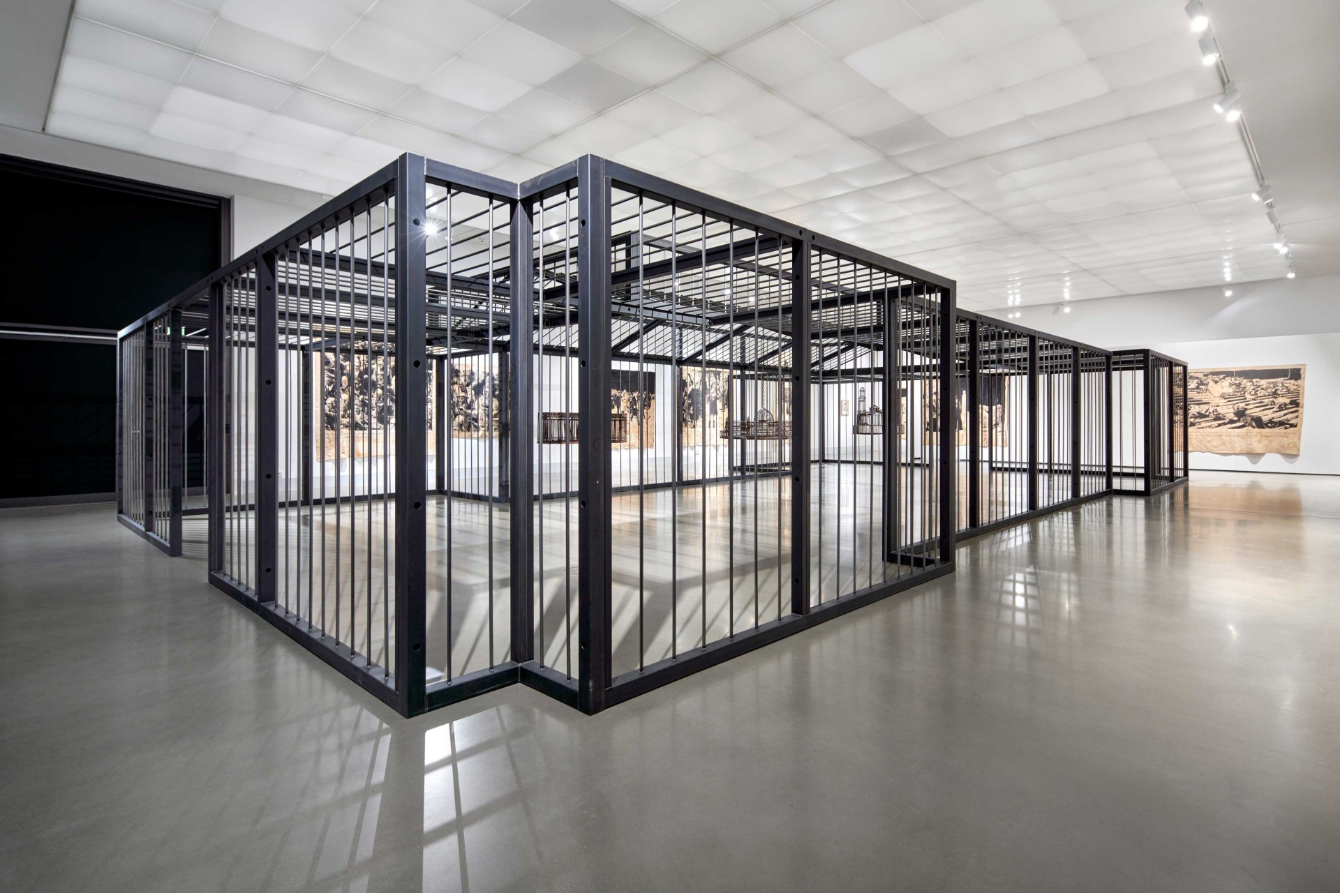 Moderne Galerie mit Metallgittern, die an ein Gefängnis erinnern, umgeben von Kunstwerken an den Wänden.