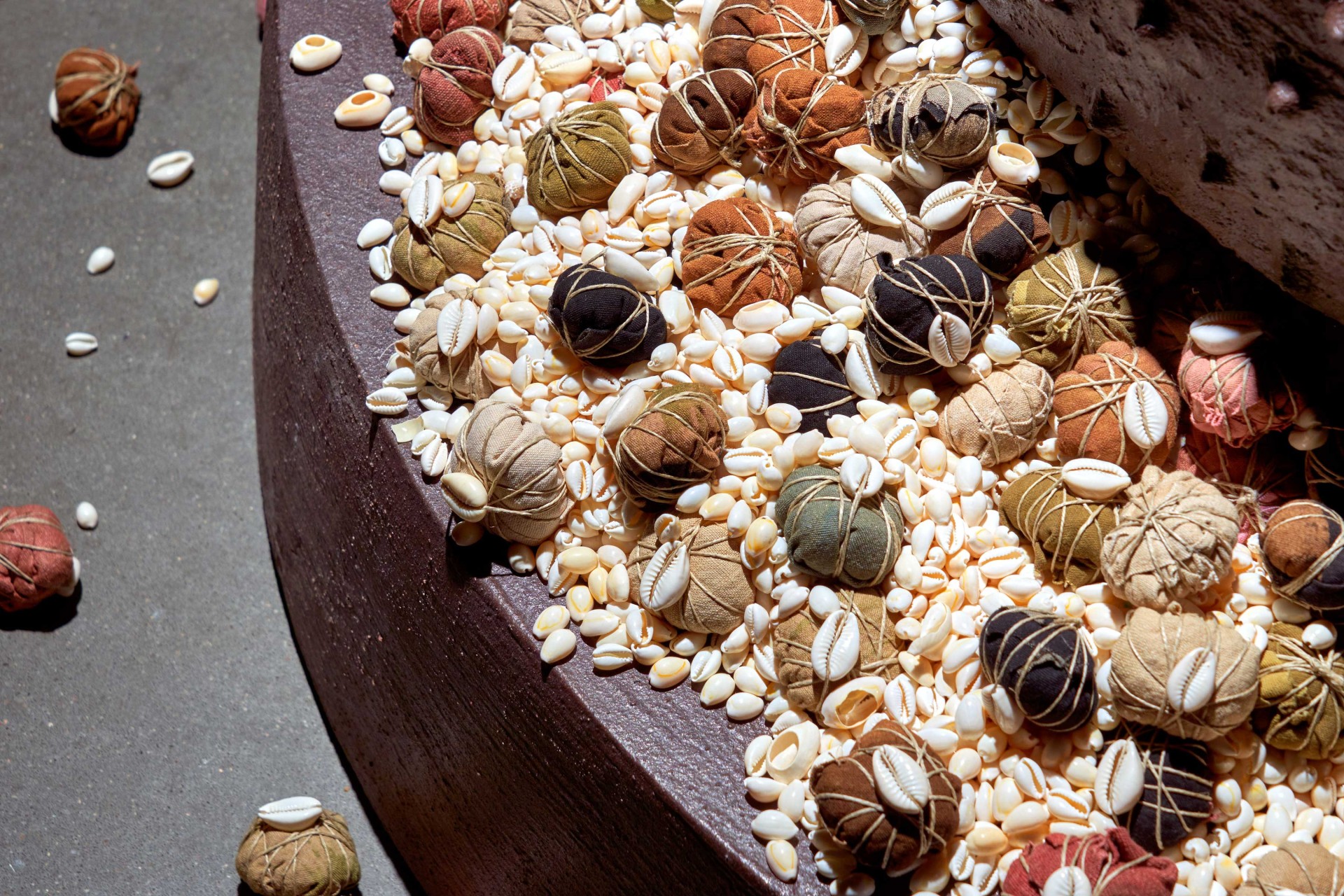 Bunte, stoffummantelte Kugeln liegen zwischen weißen Muscheln auf einer abgerundeten, dunklen Fläche.