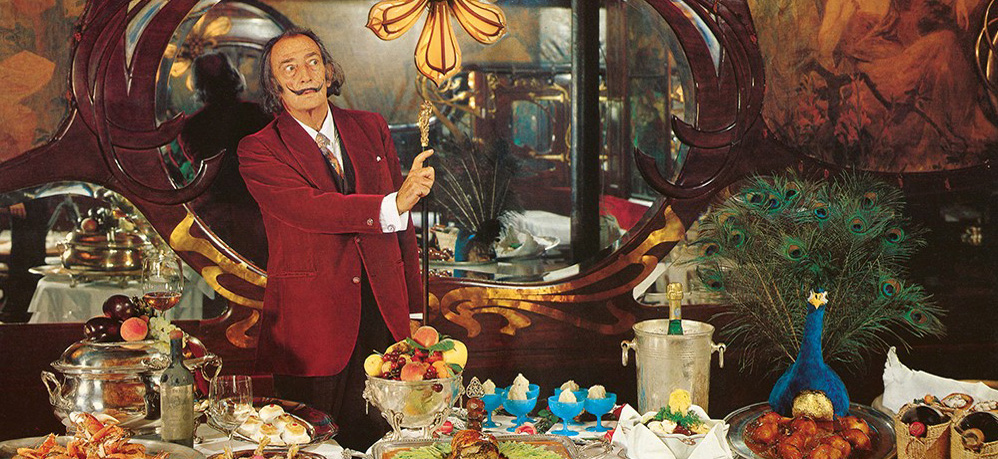 A man in a red suit presents an opulent feast, surrounded by decorative elements and a peacock.