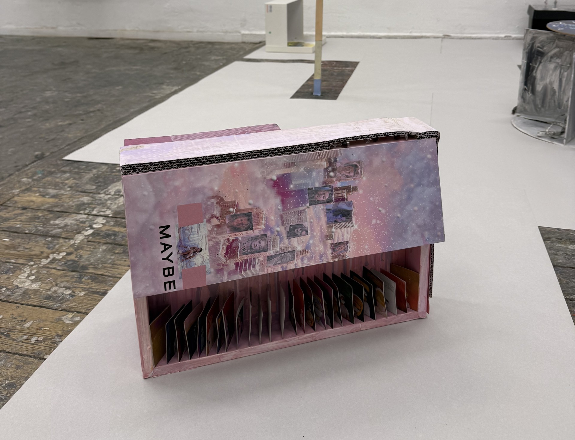 Kunstinstallation mit einem pinken Boxobjekt und einem bunten, aufrechten Stab auf hellem Boden.