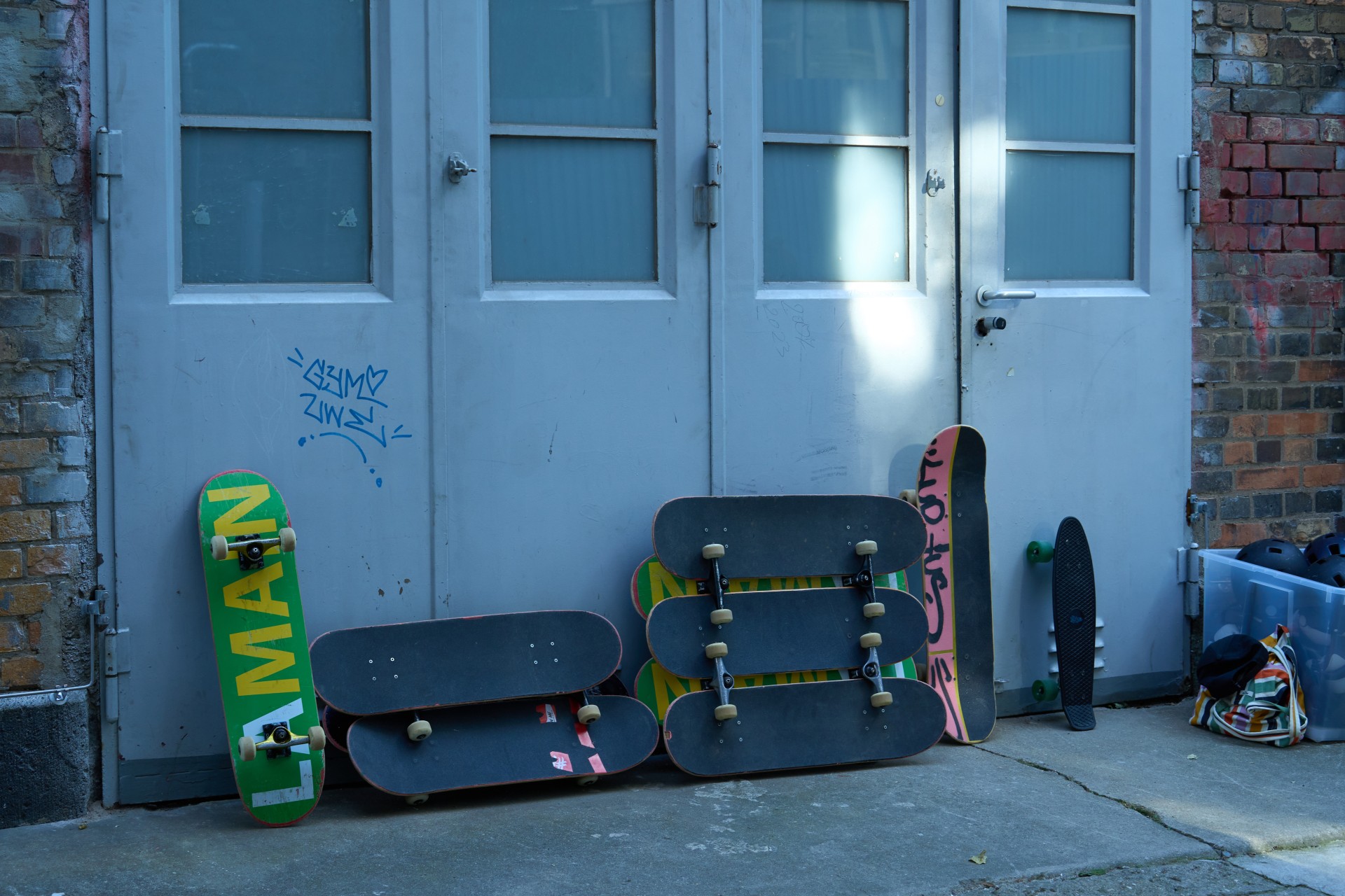 Skateboards und Helme lehnen an einer Wand neben einer grauen Tür in einer städtischen Umgebung.