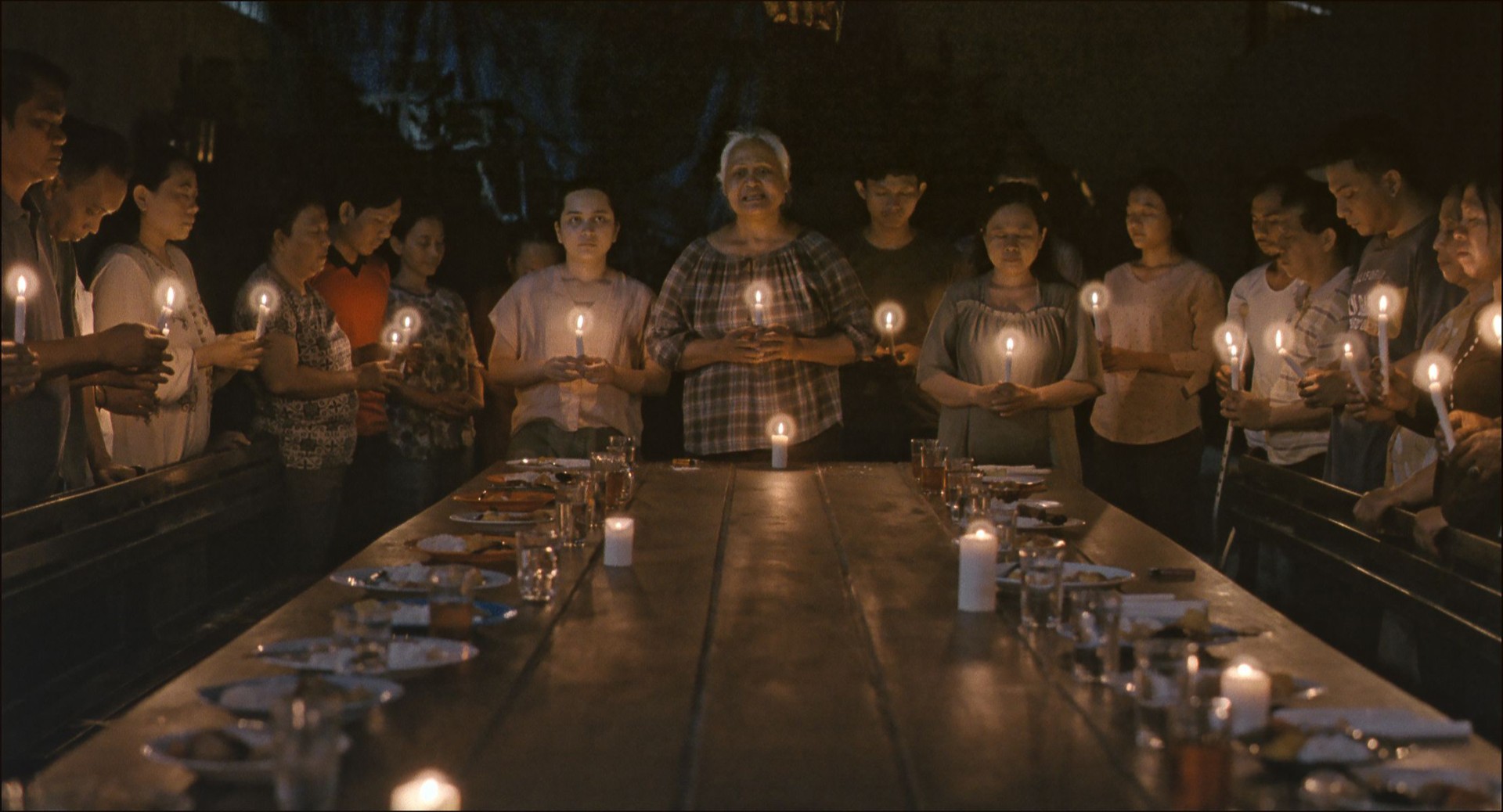 Gruppe von Menschen mit Kerzen in der Hand versammelt sich um einen Tisch in einem dunklen Raum, vermutlich für eine Zeremonie.