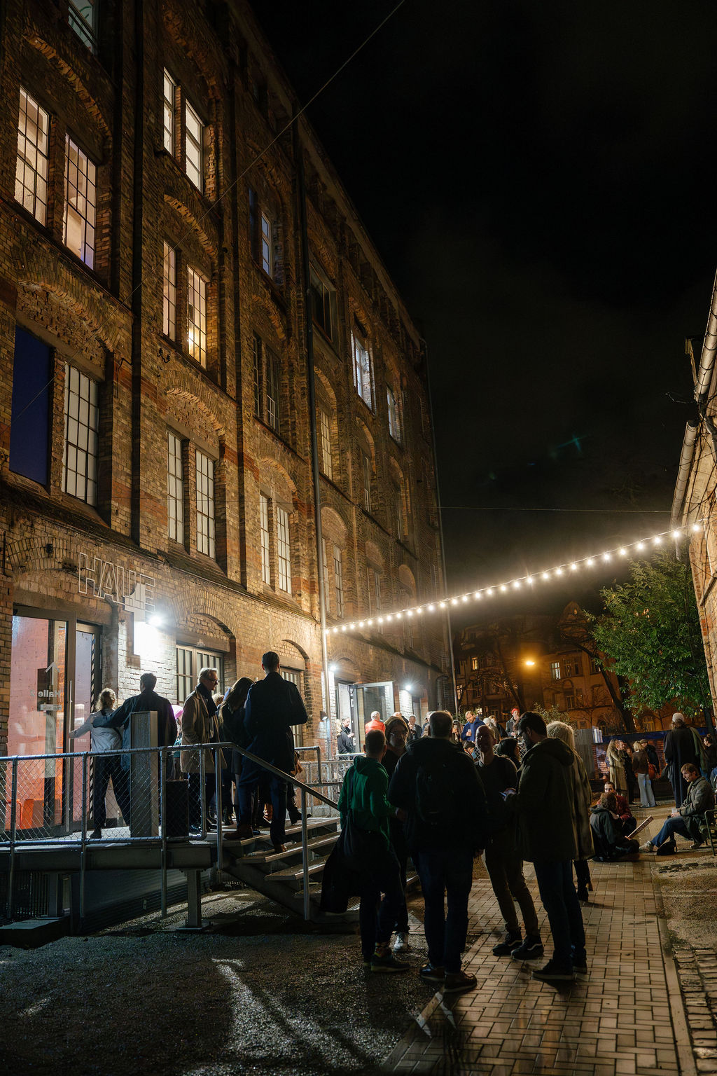 Menschen stehen nachts vor einem altehrwürdigen Backsteingebäude, beleuchtet von Lichtern und Fenstern.