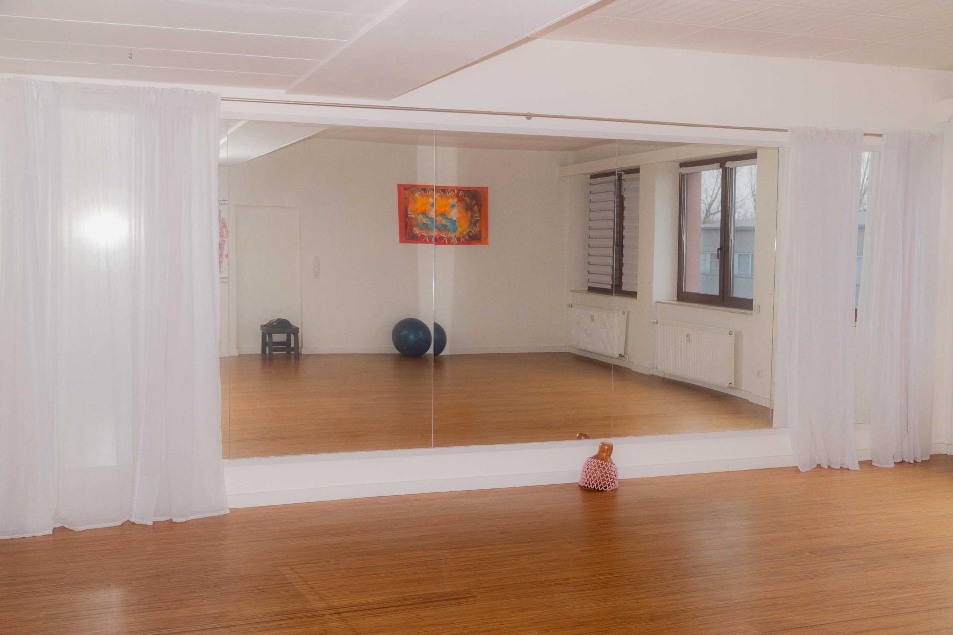 Heller Raum mit Spiegel, Holzboden, Kunstwerk an der Wand, Gymnastikball und dekorativer Figur.