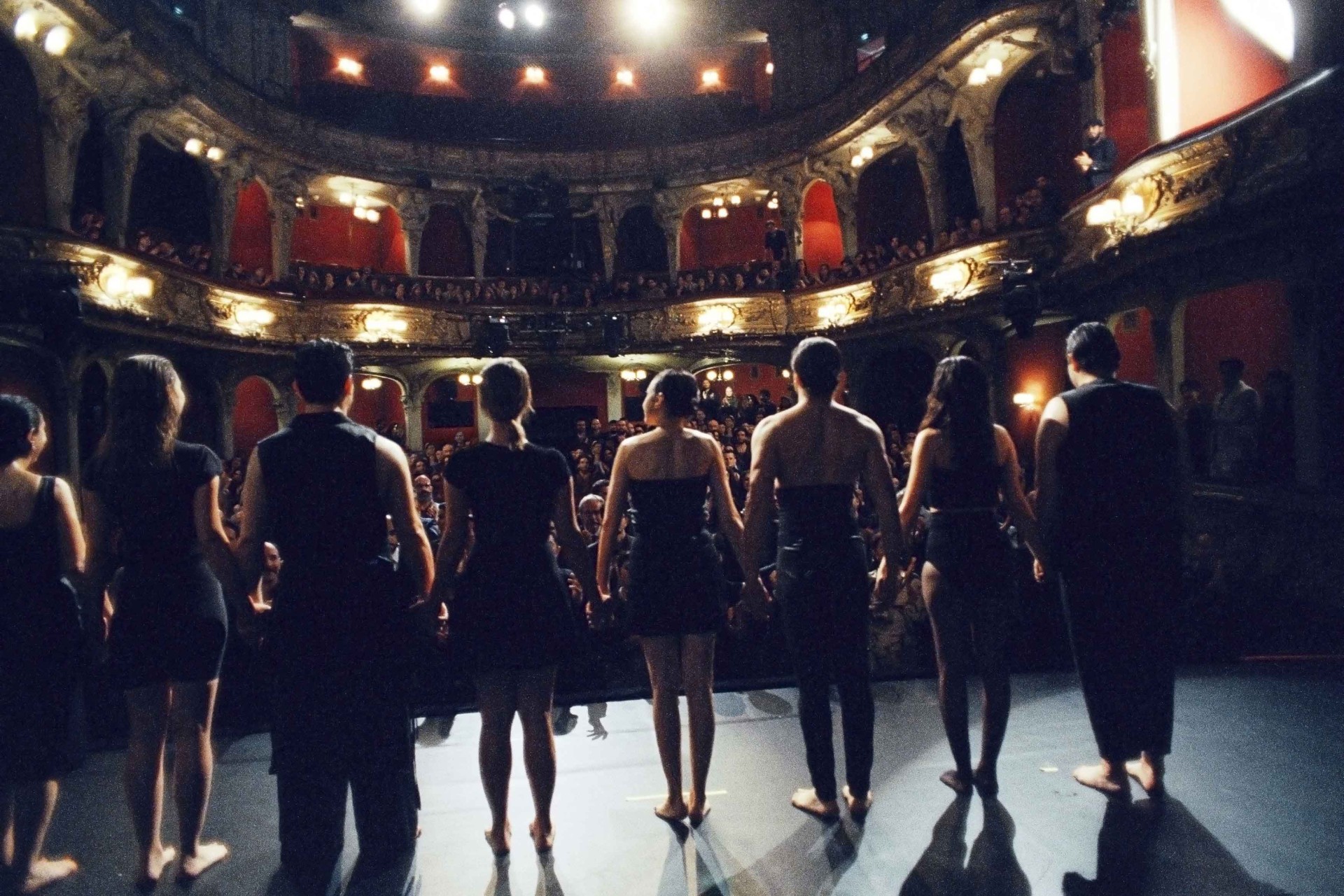 Bühnenansicht mit Tänzern, die sich umarmen, vor einem Publikum in einem eleganten Theater.