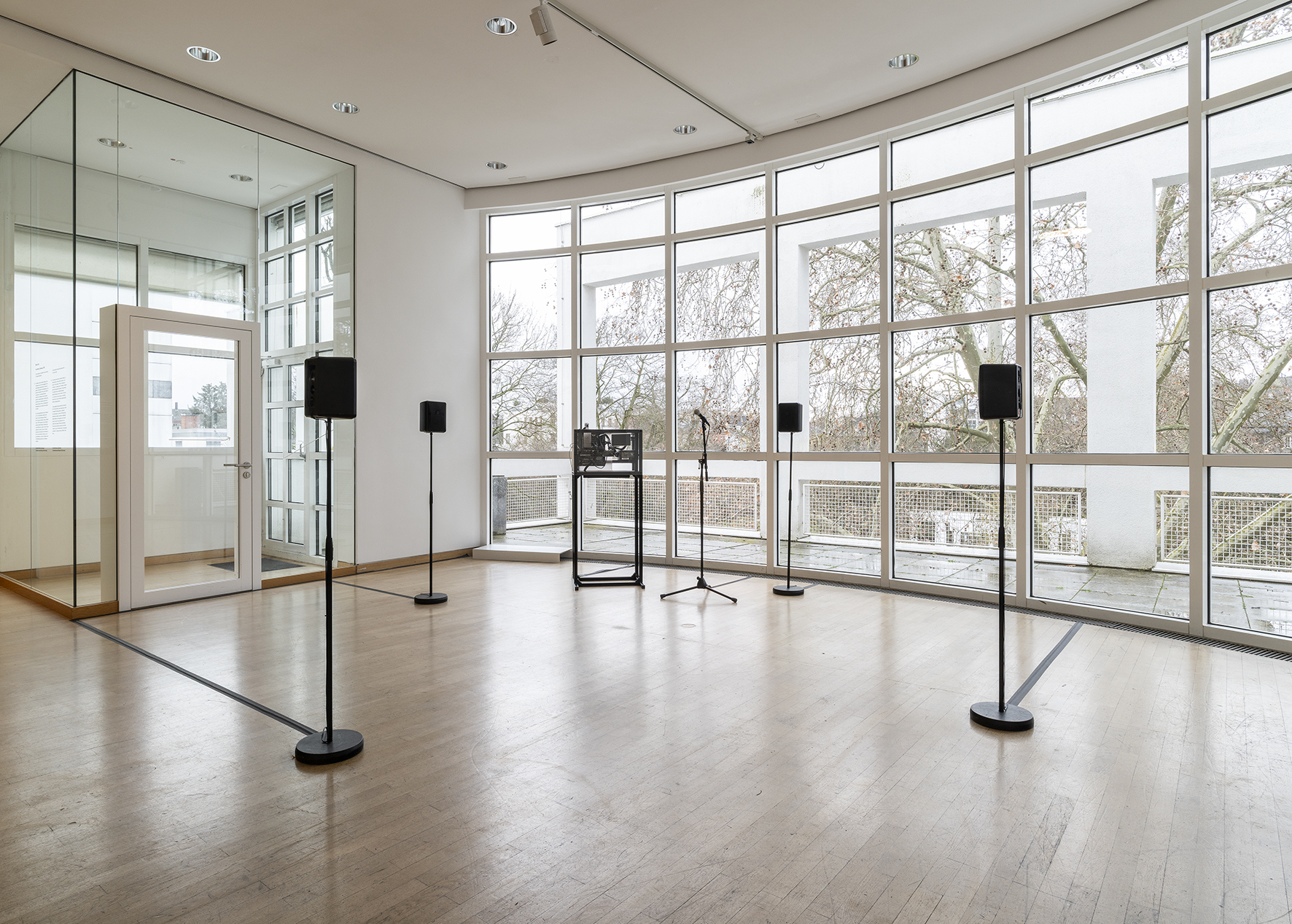 Kunstraum mit großen Fenstern, Mikrofonen und Lautsprechern für eine Klanginstallation. Minimalistische Einrichtung.