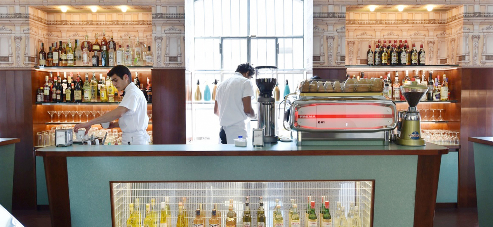 Zwei Barkeeper in einer stilvollen Bar, umgeben von zahlreichen Getränken und Gläsern.